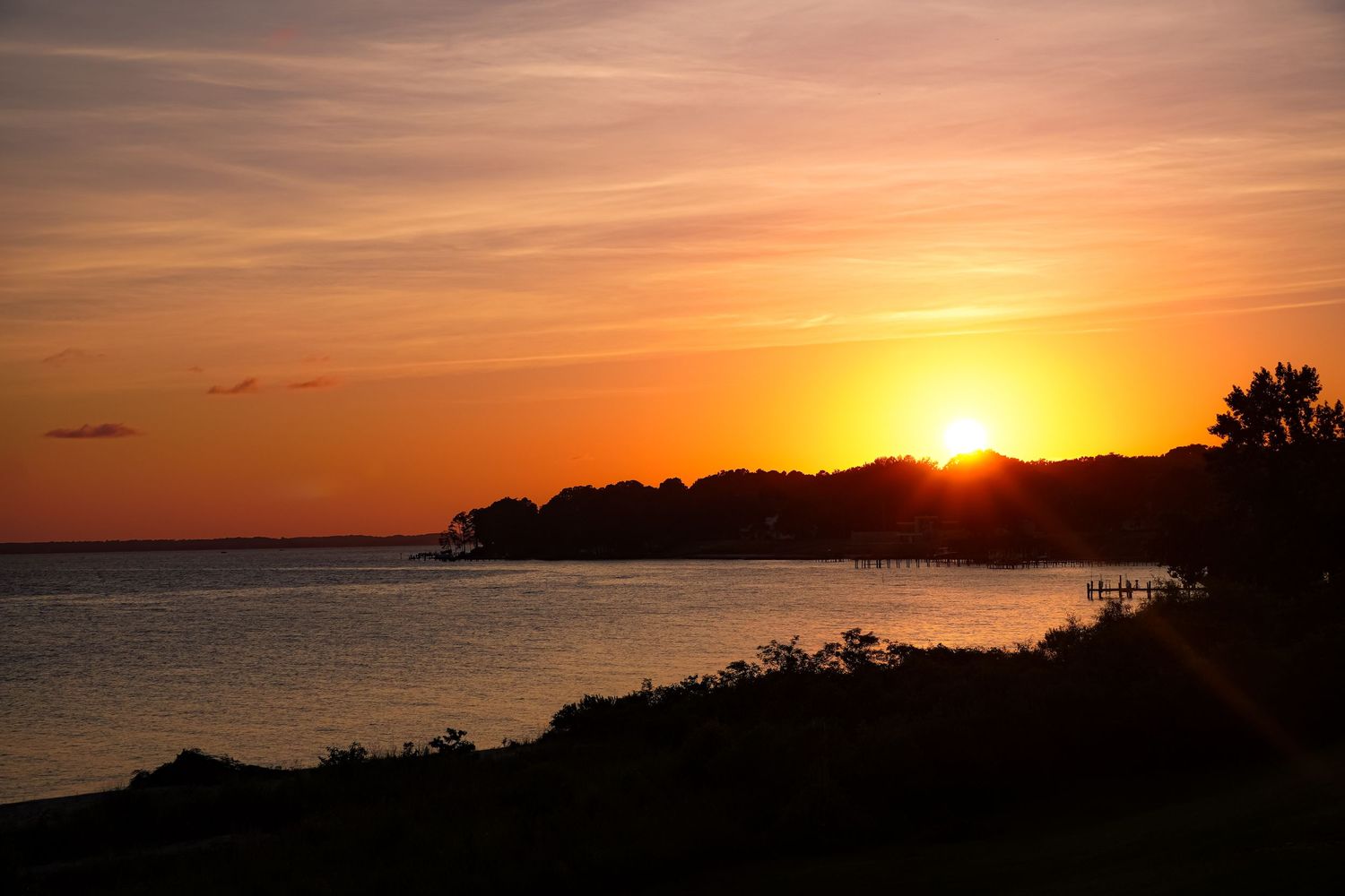 A stunning orange sunset silhouettes the coastline with a pier extending into the calm waters.