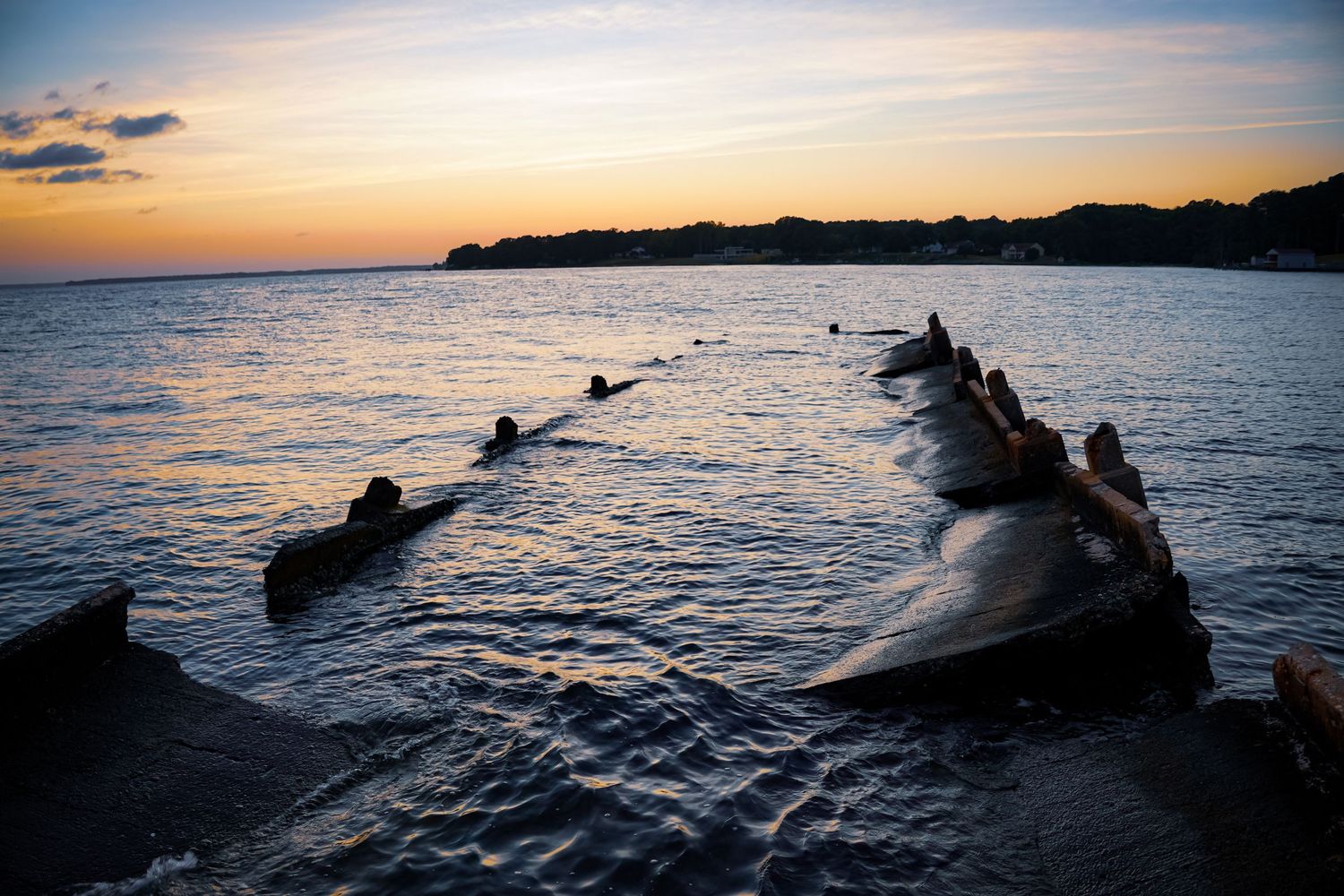 Rocky breakwater extends into the ocean during a peaceful sunset with dramatic sky colors.