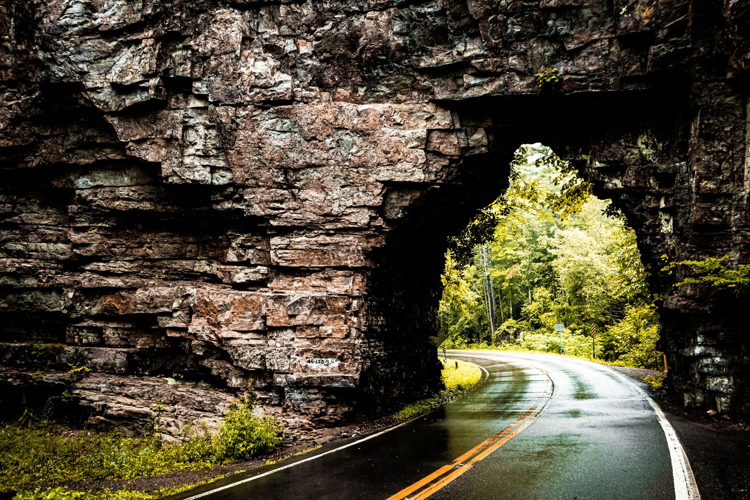 A winding mountain road curves through a scenic forest with sunlight filtering through the trees.