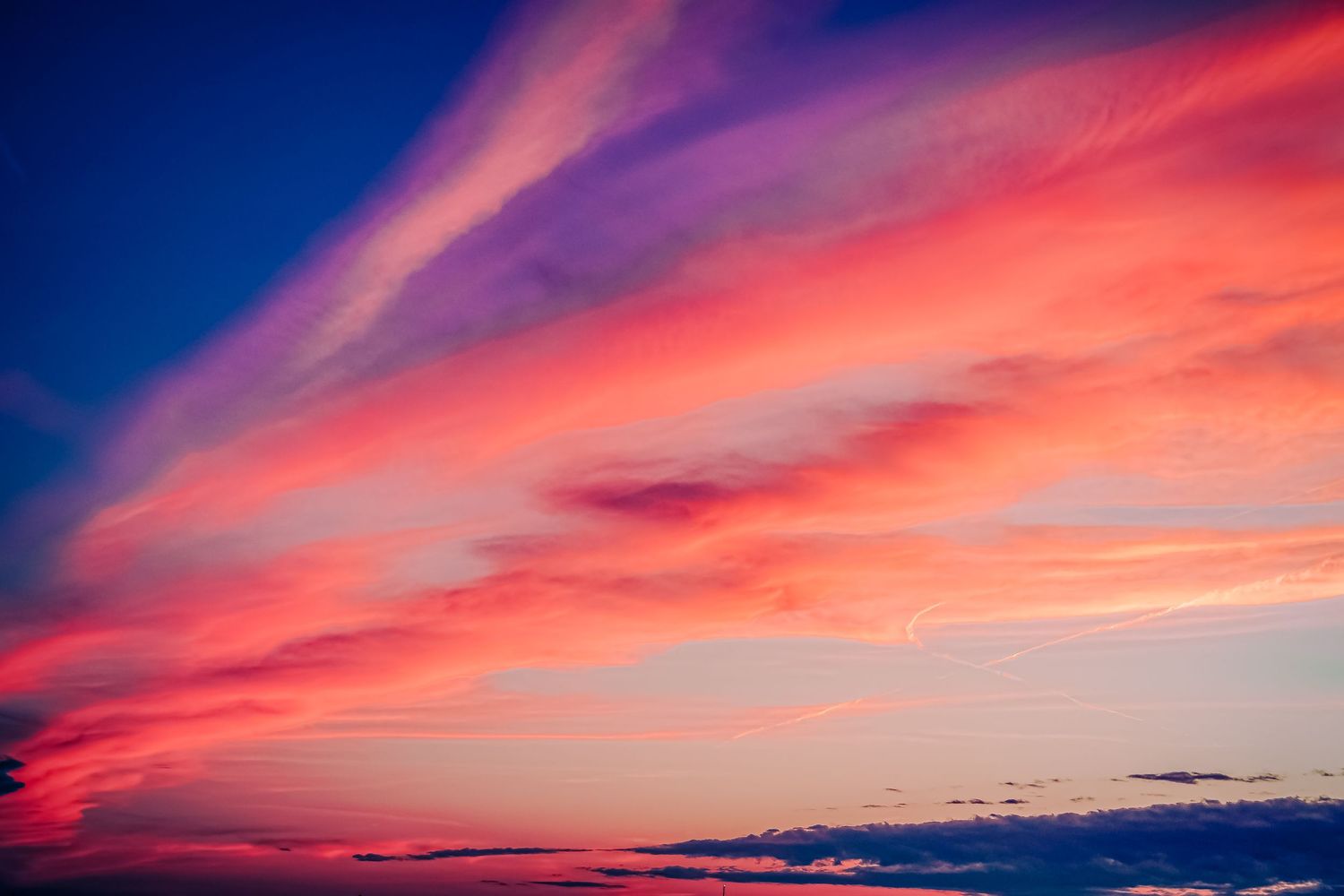 Dramatic sunset sky with vibrant pink and purple clouds against deep blue background.