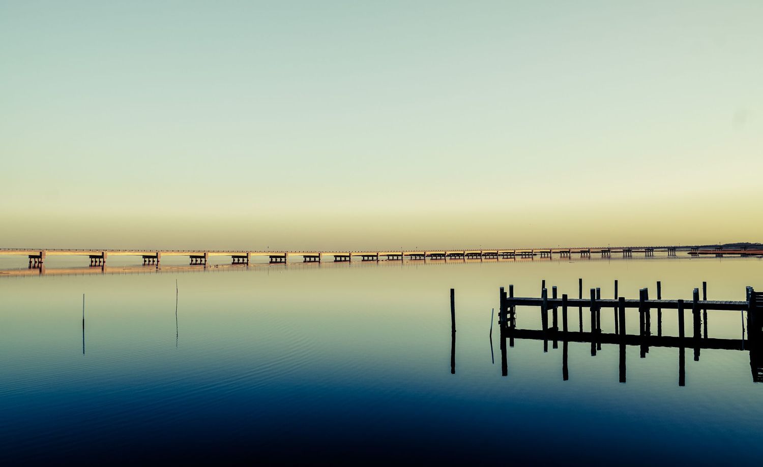 Minimalist pier and dock silhouettes on perfectly calm water at dusk.