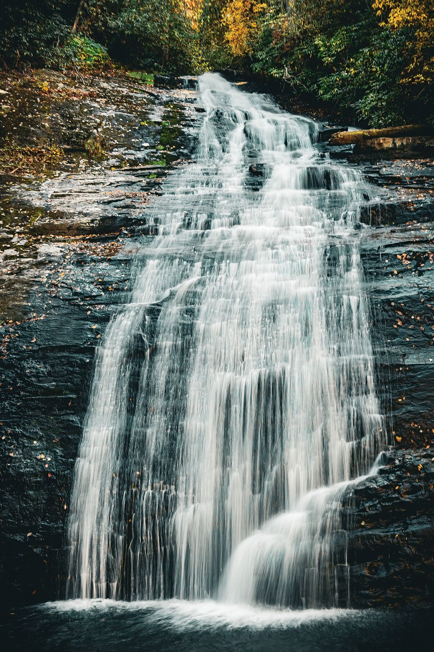 A majestic waterfall cascades down rocky cliffs surrounded by autumn foliage.