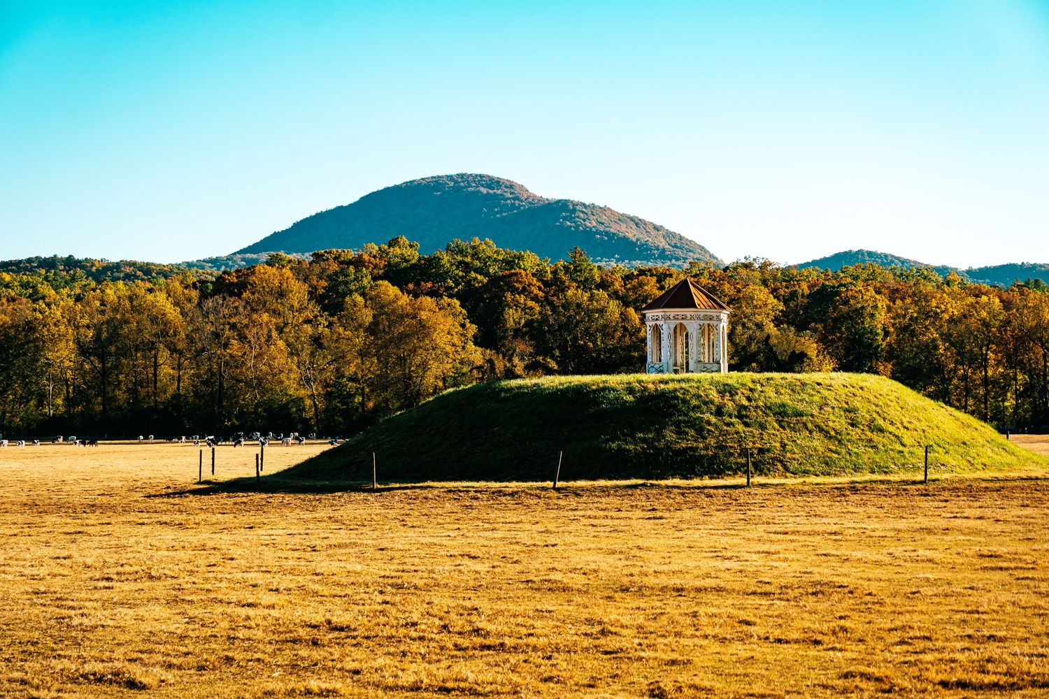 Historic white gazebo perched atop grassy hill with mountain backdrop during autumn.
