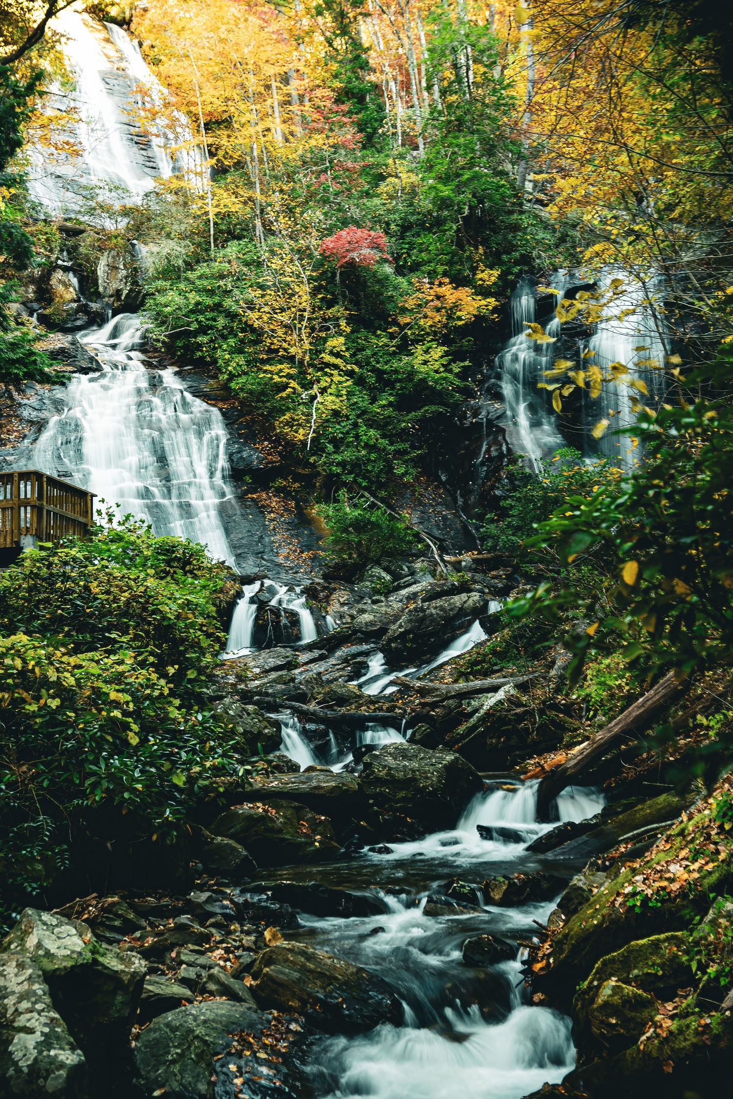 Multi-tiered waterfall cascading through autumn forest with observation deck and vibrant fall colors.