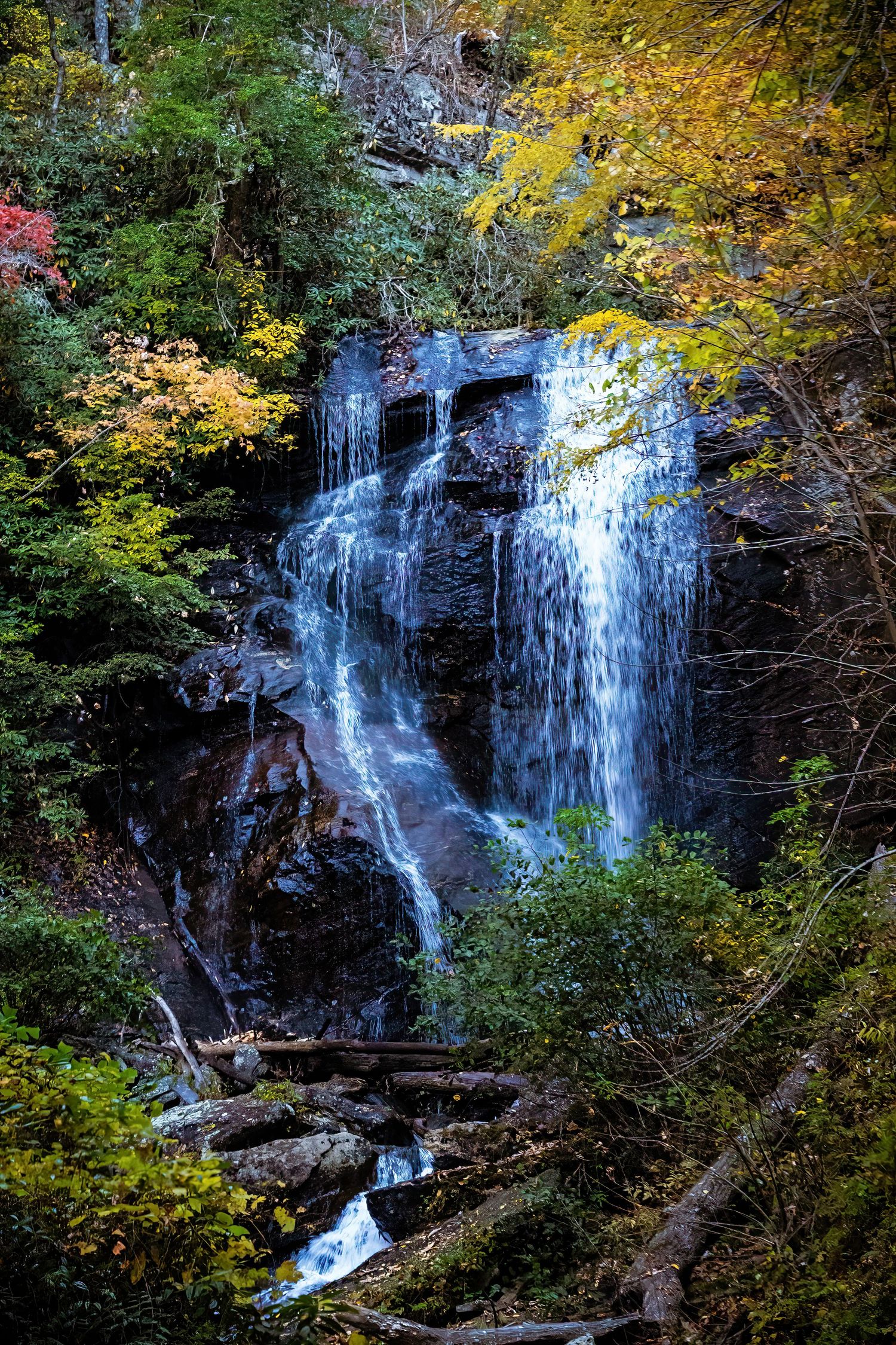 Majestic waterfall flowing over rocky cliff face framed by colorful fall foliage.