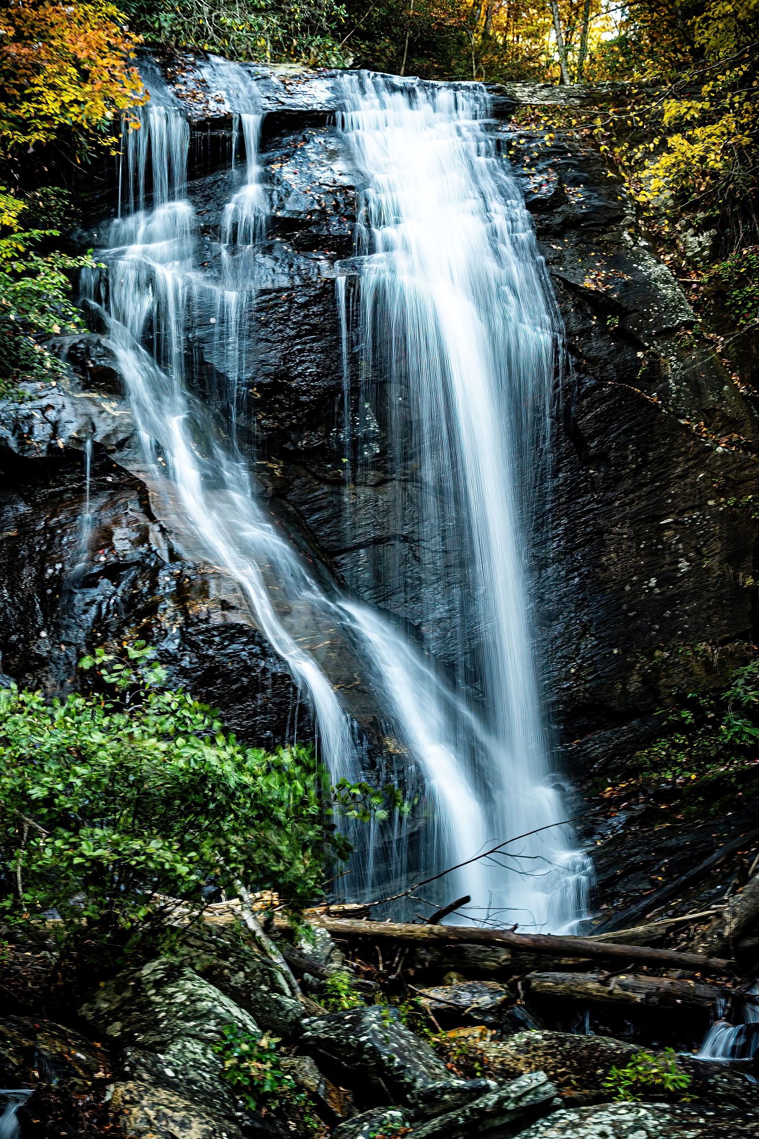 Tall waterfall streaming down dark rocky cliff face with green vegetation.