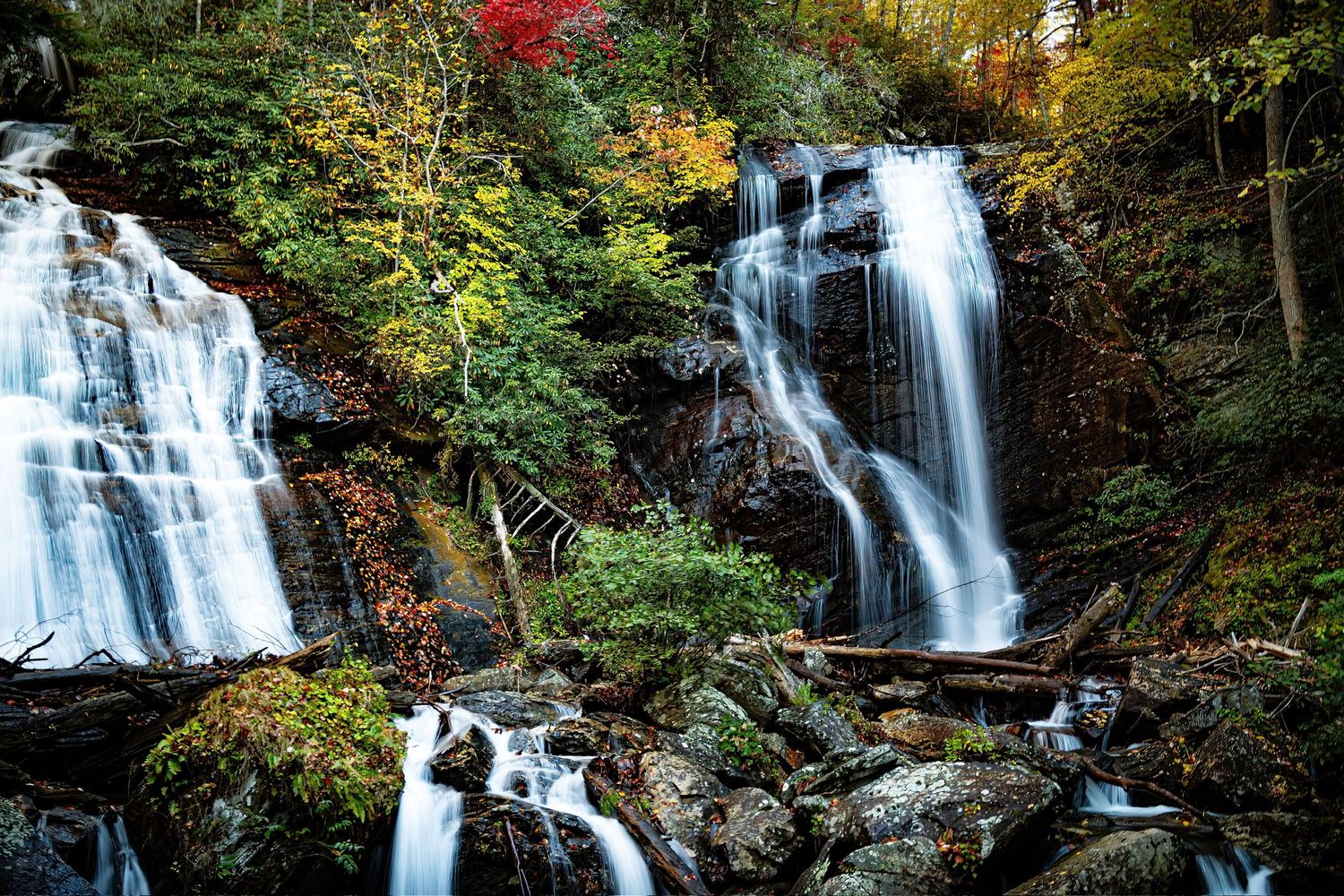 Twin waterfalls flowing over rocky cliffs surrounded by vibrant autumn colors.