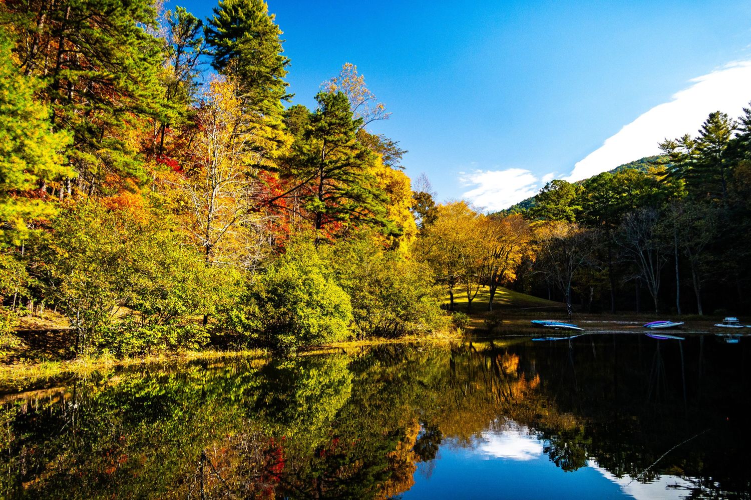 Fall colors reflect perfectly in a calm lake surrounded by autumn trees under blue skies.