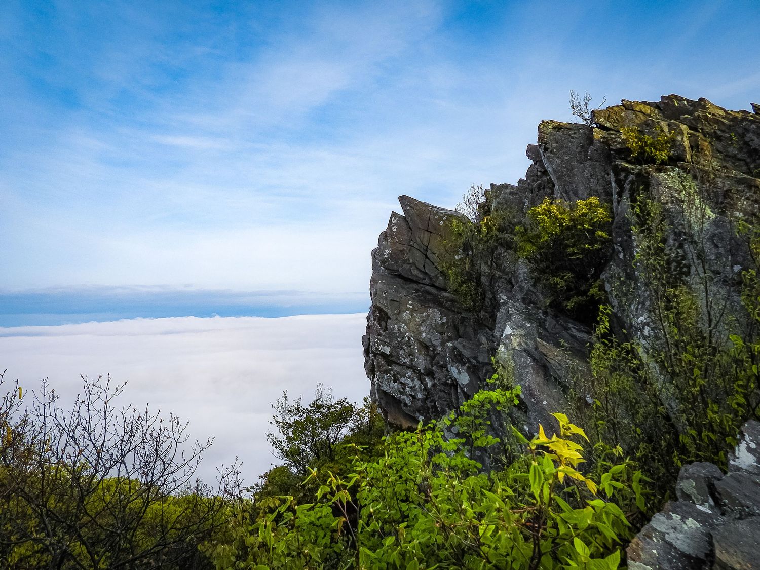 Steep rocky cliff edge overlooking a misty valley under blue skies.