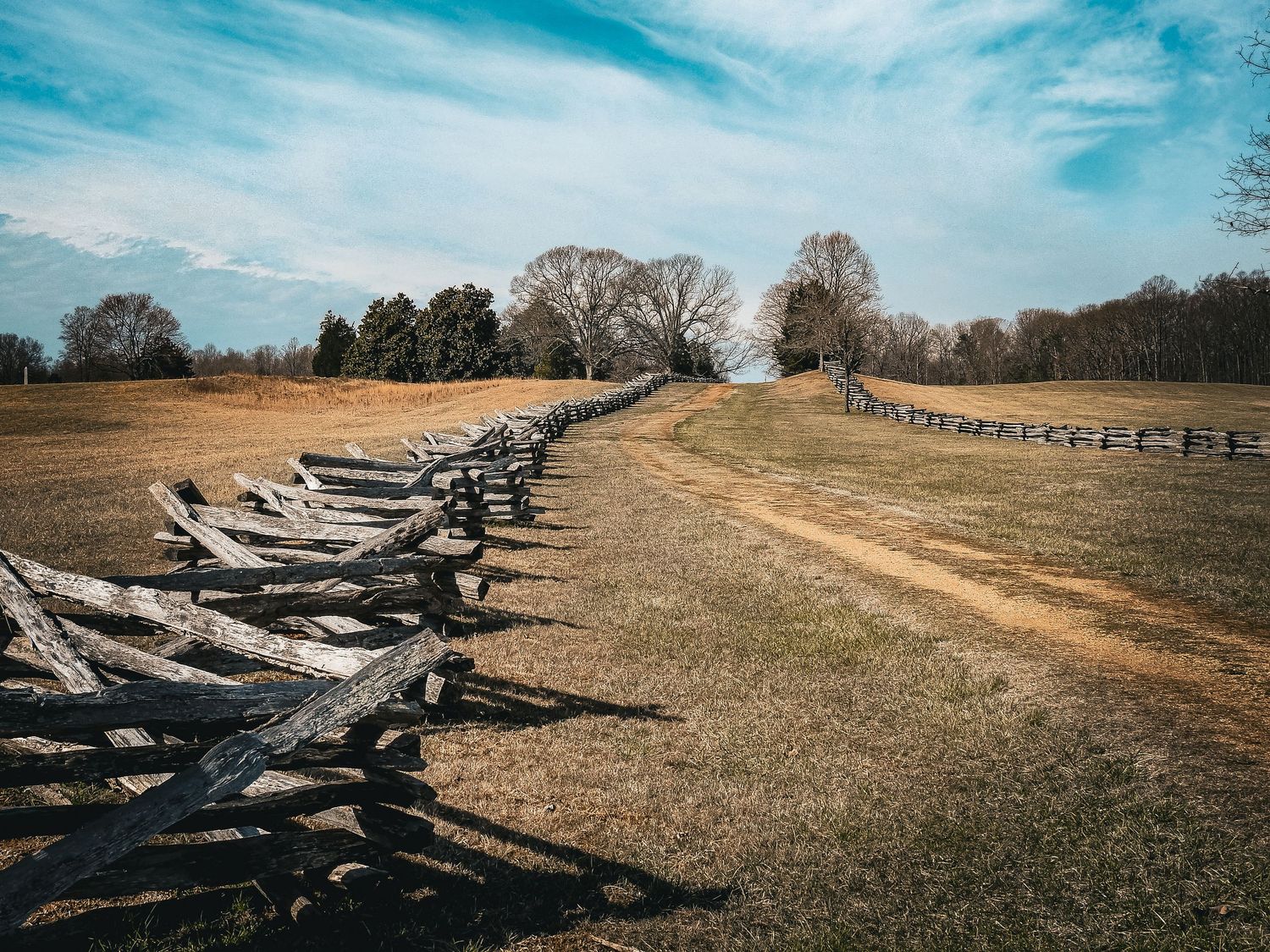 Rustic wooden split-rail fence stretching across brown grass field under blue sky.