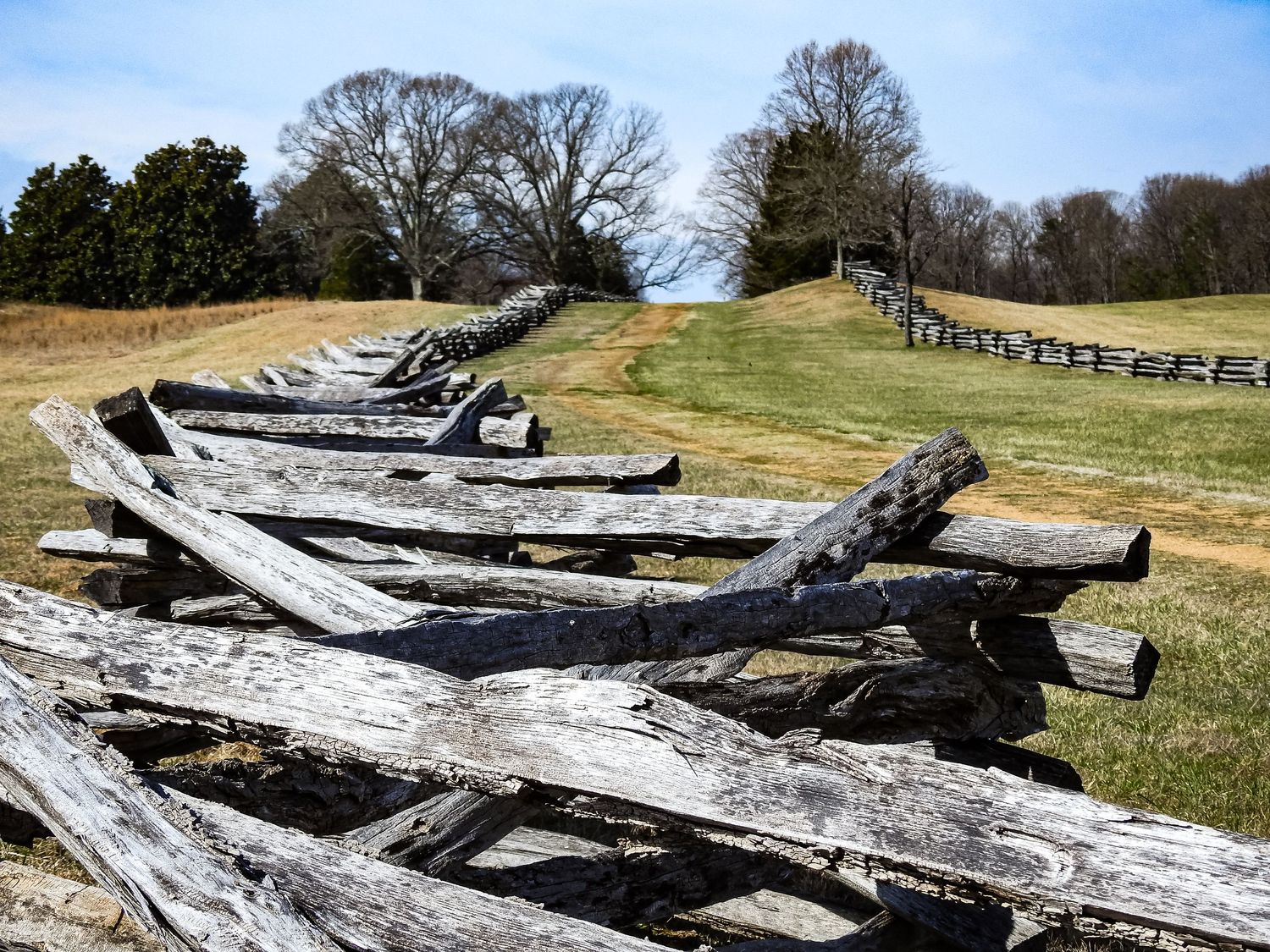 Weathered wooden fence rails stacked in layers on a grassy hillside with trees in the background.