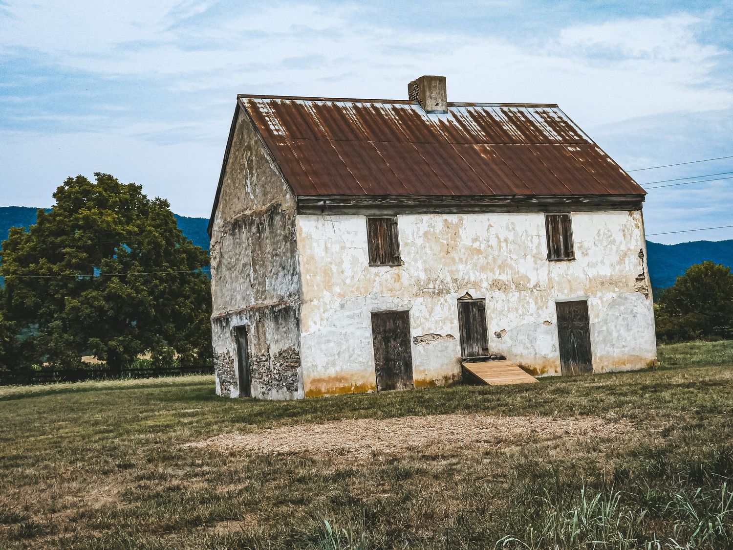 Abandoned stone farmhouse with weathered walls standing alone in a grassy field.