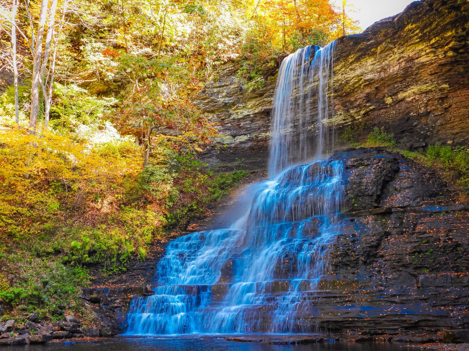 Majestic waterfall cascading down rocky cliffs surrounded by vibrant autumn foliage.