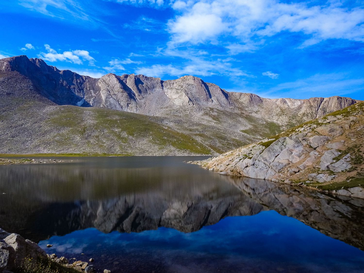 Mountain lake reflecting rugged peaks and blue sky in a pristine alpine landscape.