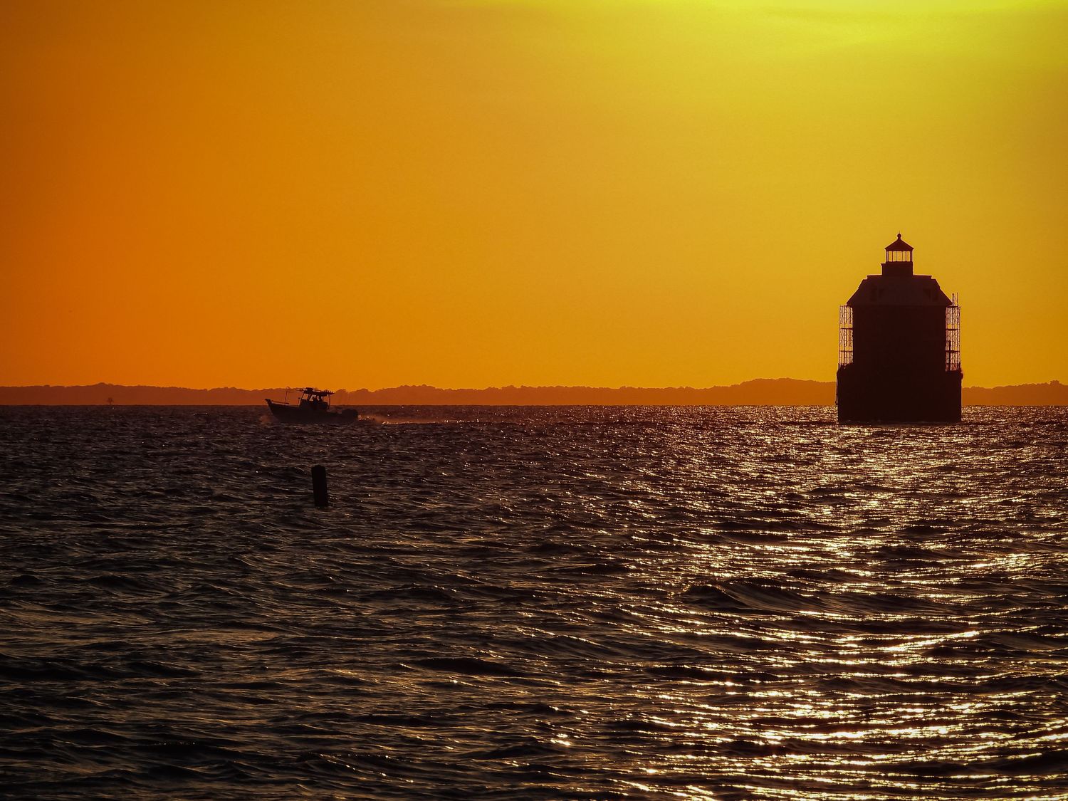 Silhouette of lighthouse against golden sunset sky over dark rippling waters.