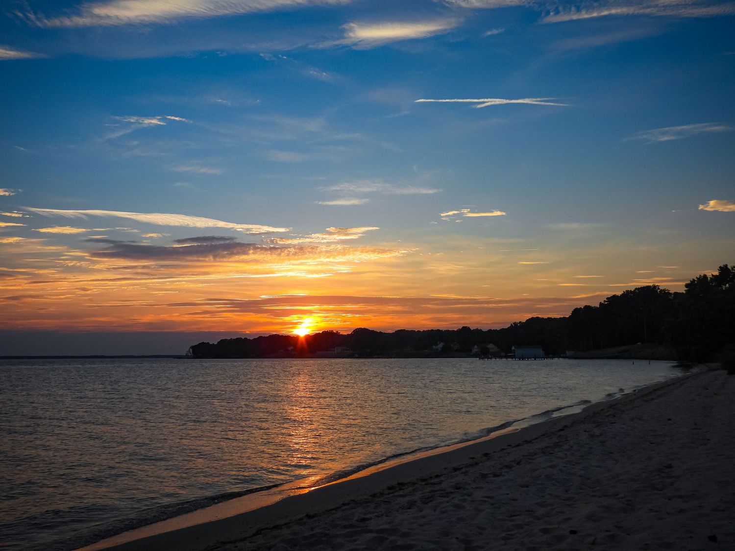 Dramatic orange sunset over a calm beach with silhouetted shoreline and scattered clouds in the sky.