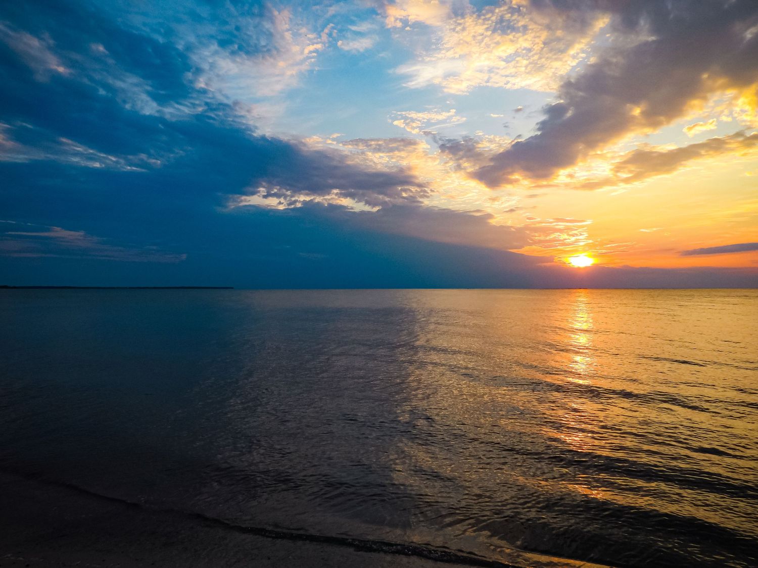 Golden sunset reflects on rippling ocean waters under dramatic cloudy sky.