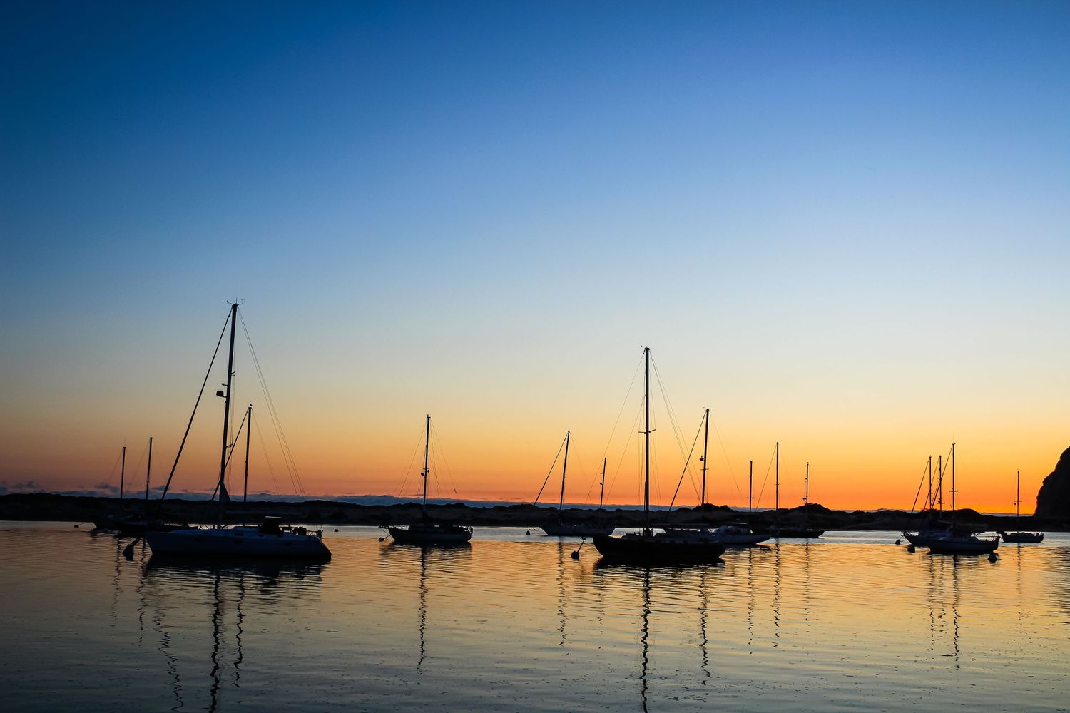 Sailboats silhouetted against a vibrant orange and blue sunset sky at harbor.