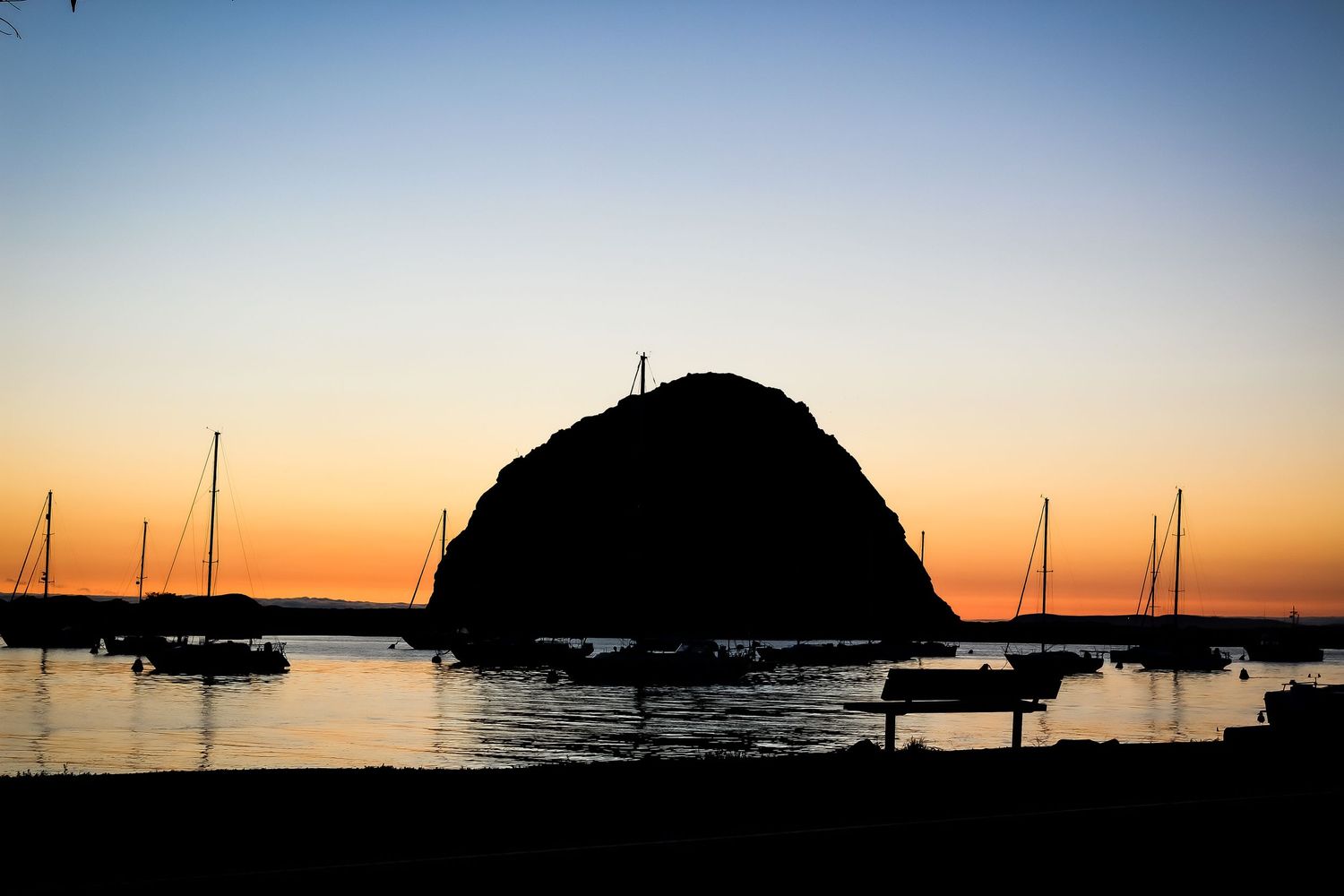 Dramatic silhouette of Morro Rock against golden sunset with boats in the foreground.