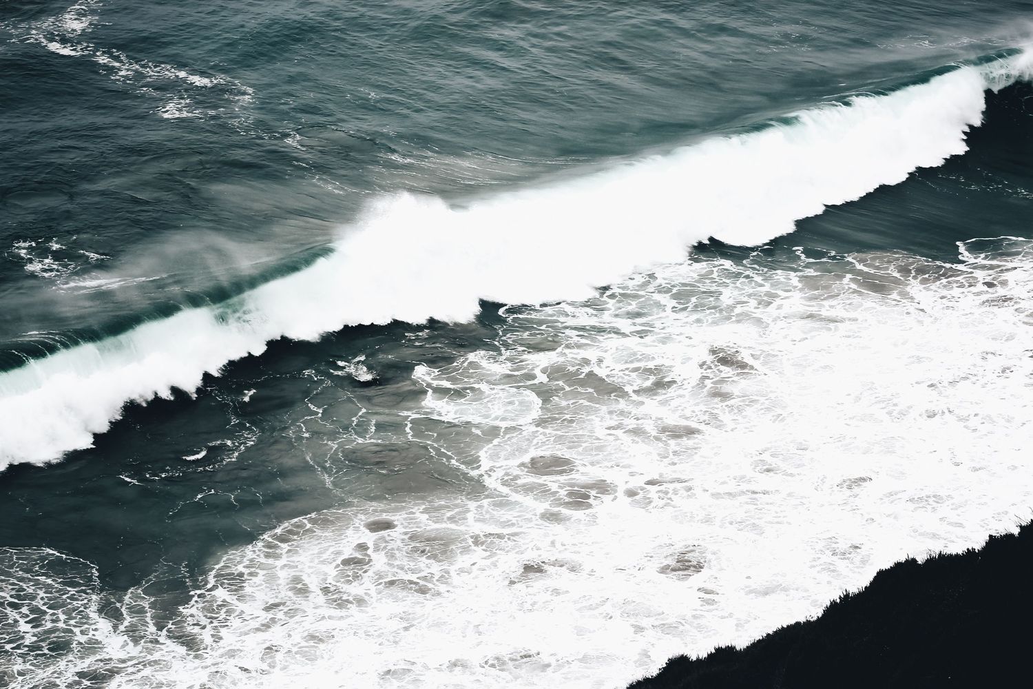 Aerial view of powerful ocean waves breaking with white foam against dark waters.