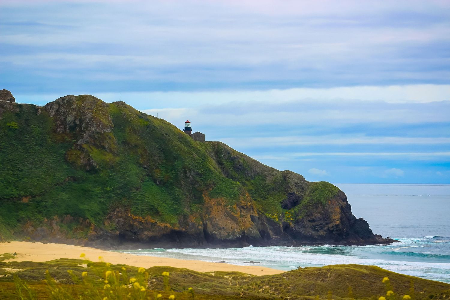 Dramatic coastal landscape with green cliffs overlooking a secluded beach and blue ocean waters.