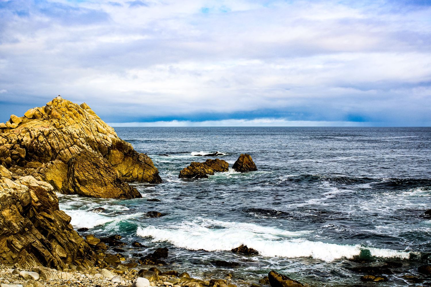 Rocky coastline with crashing waves against golden cliffs under cloudy skies.