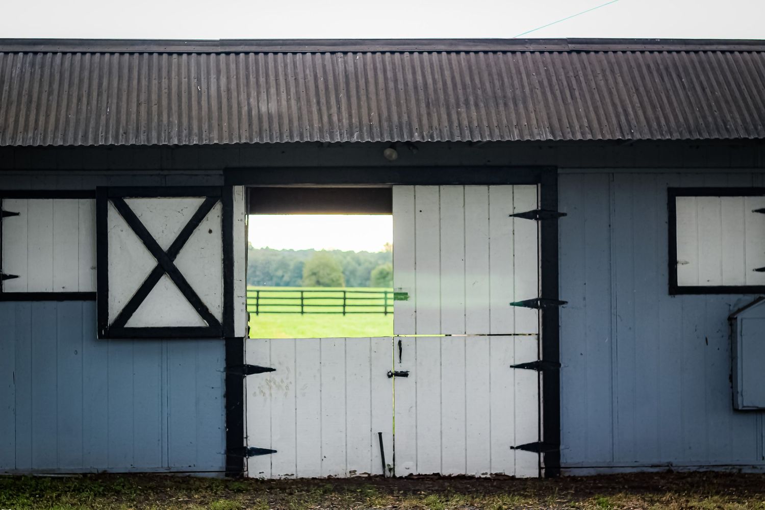 White barn door with cross beams frames a green pasture view.