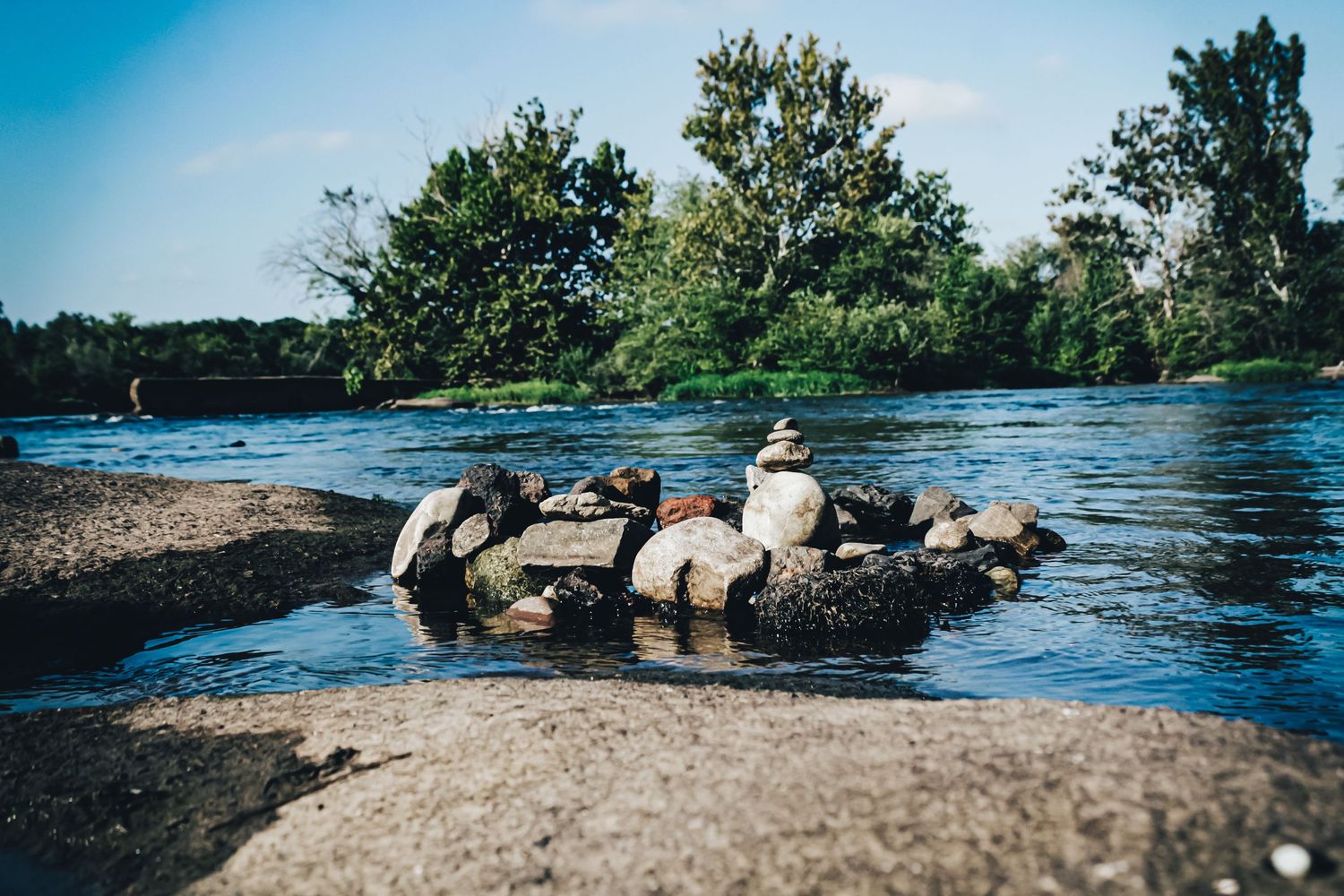 Rock formations in a flowing river with trees lining the shoreline.