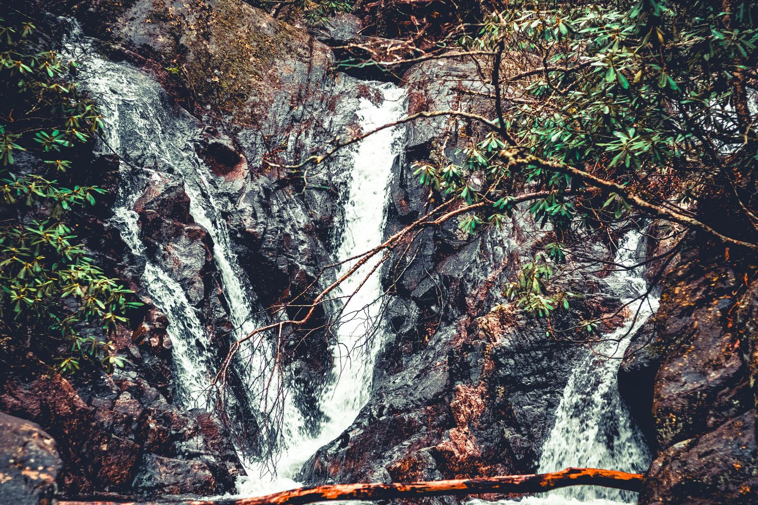 A cascading waterfall flows down dark rocky cliffs surrounded by autumn foliage and moss-covered stones.