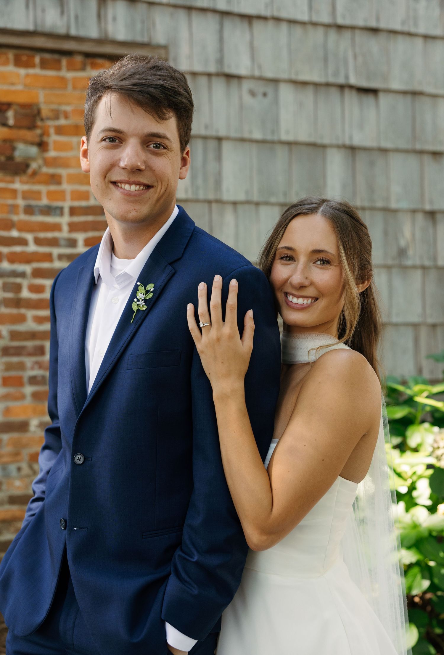 Joyful wedding couple posing in front of rustic wooden wall showing off engagement ring in series of candid shots.