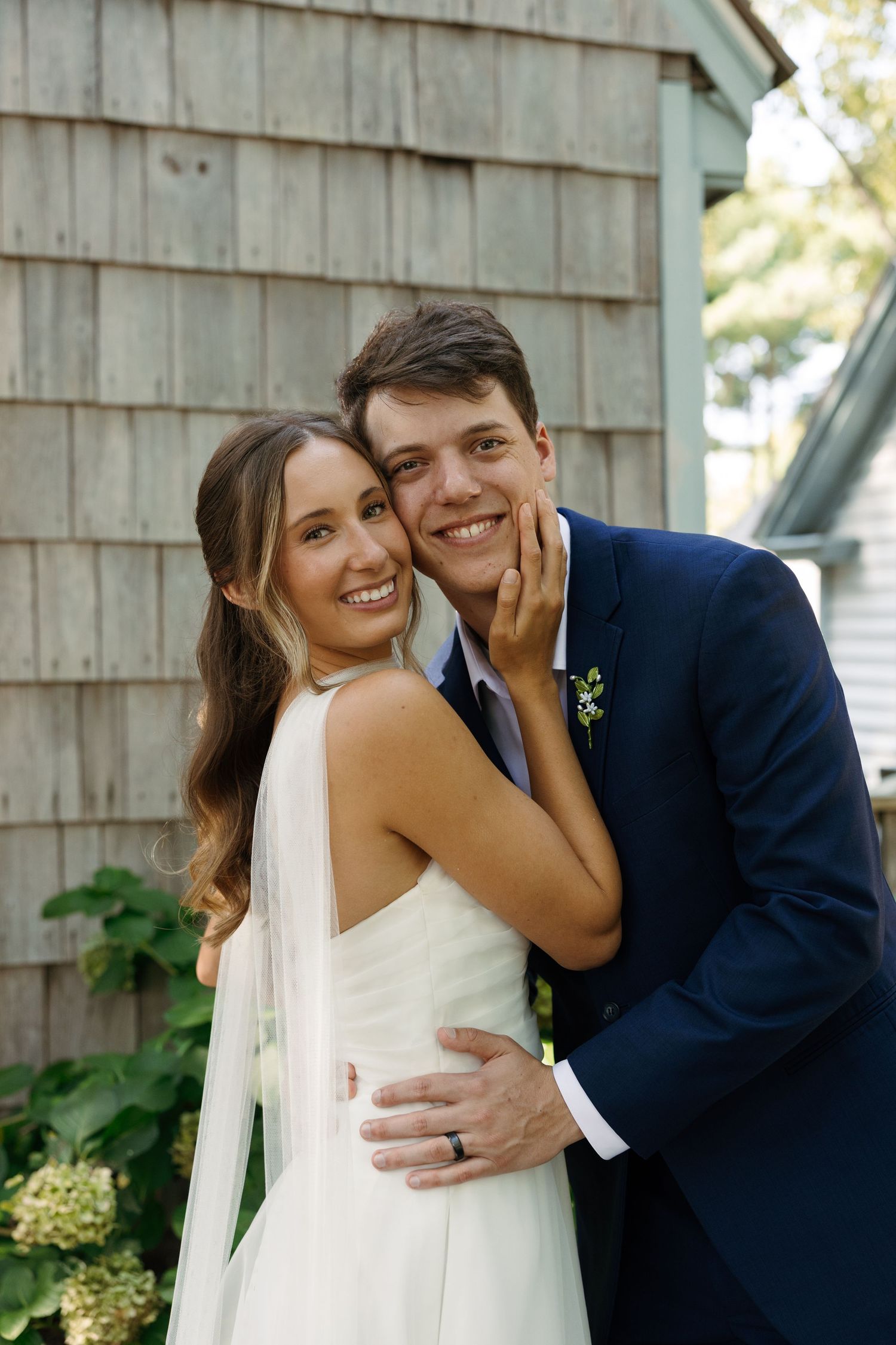 Happy newlyweds share intimate moments and laughter while posing against weathered wood siding.