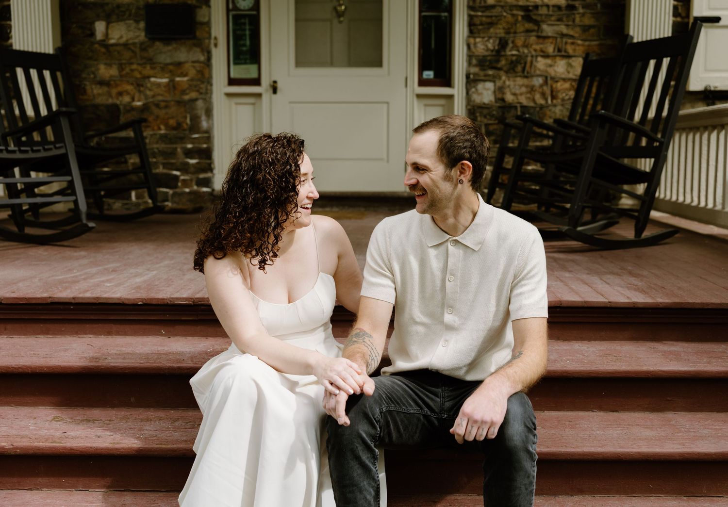 Couple sitting on wooden porch steps in casual wedding attire.