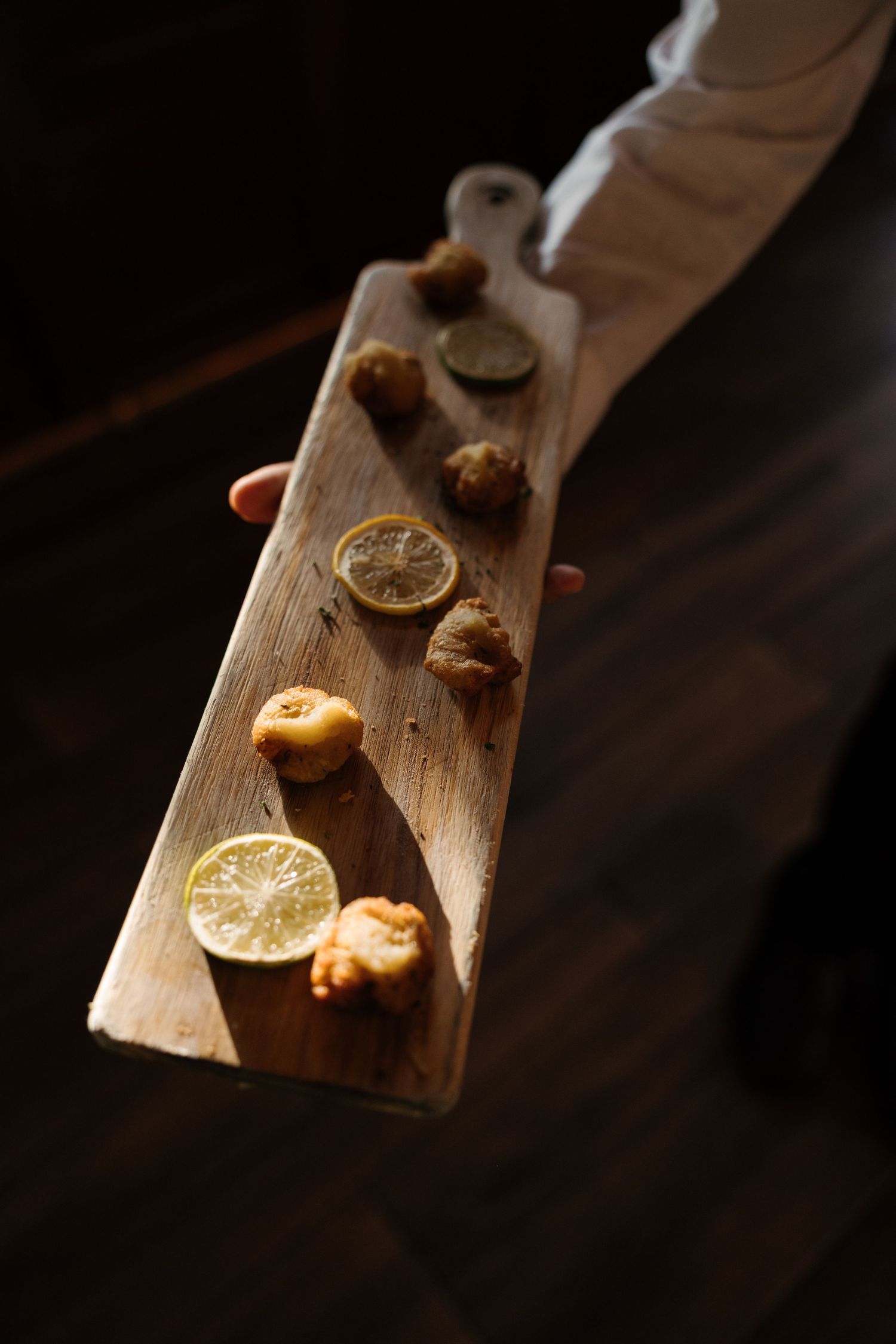 Server holding rustic wooden board with fried appetizers and sliced citrus lemons and limes.
