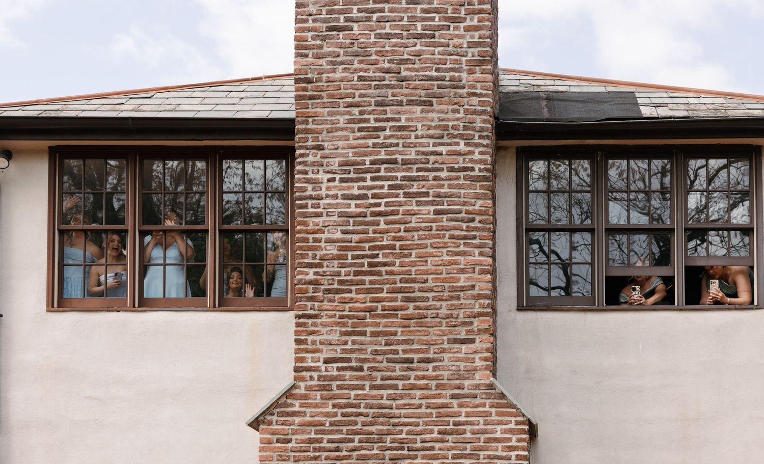 Brick chimney on a stucco building with brown-framed windows reflecting trees and blue sky.