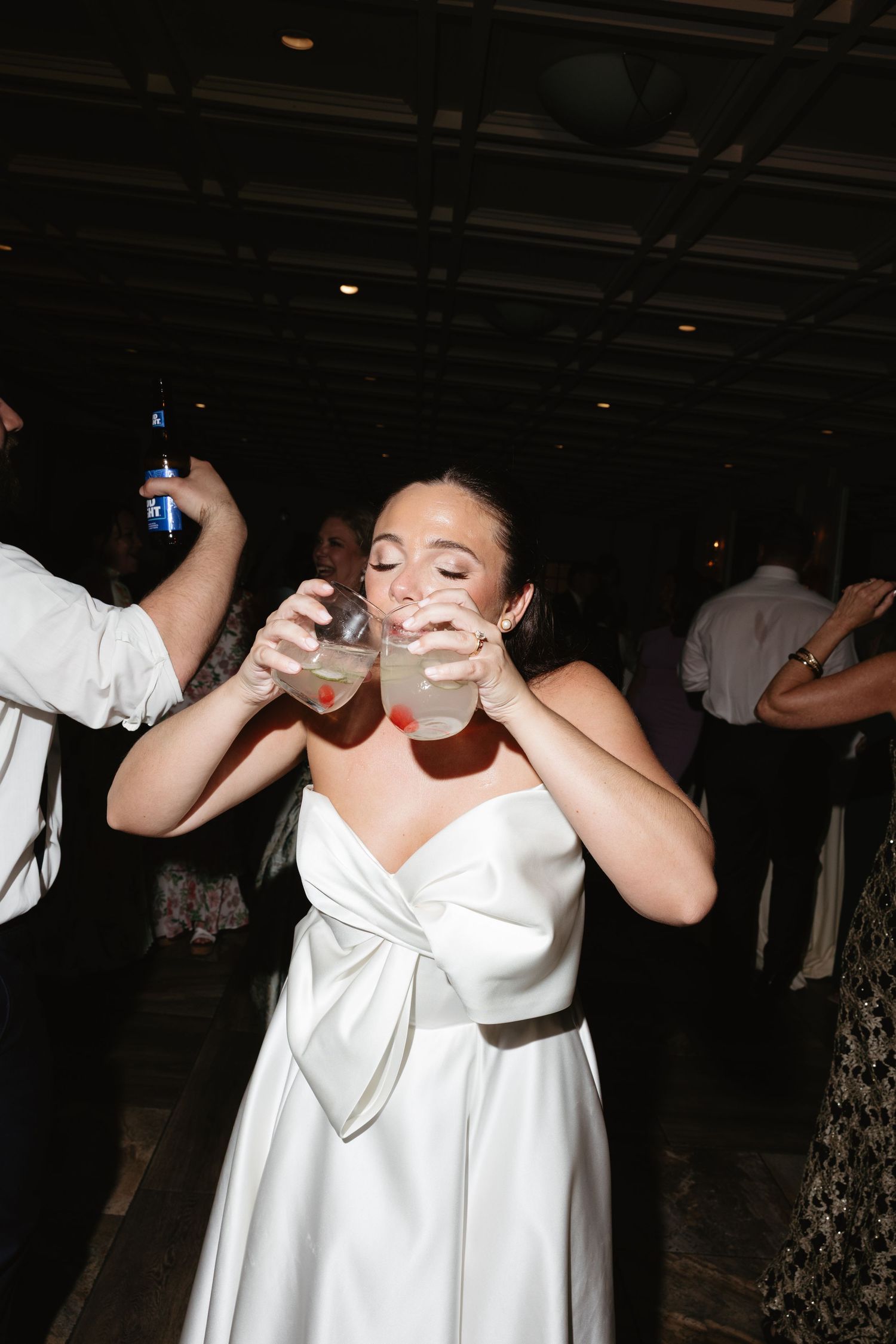 Bride in white satin gown drinking cocktails on the dance floor at her wedding reception.