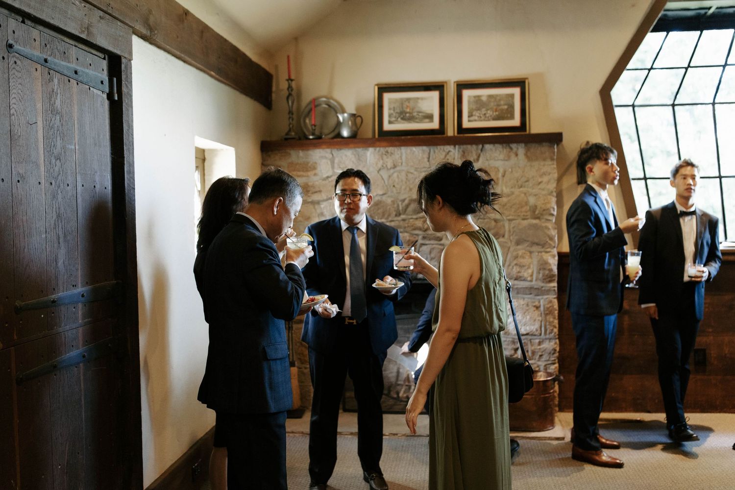 Wedding guests mingling in a rustic indoor venue with stone walls and wooden beams.