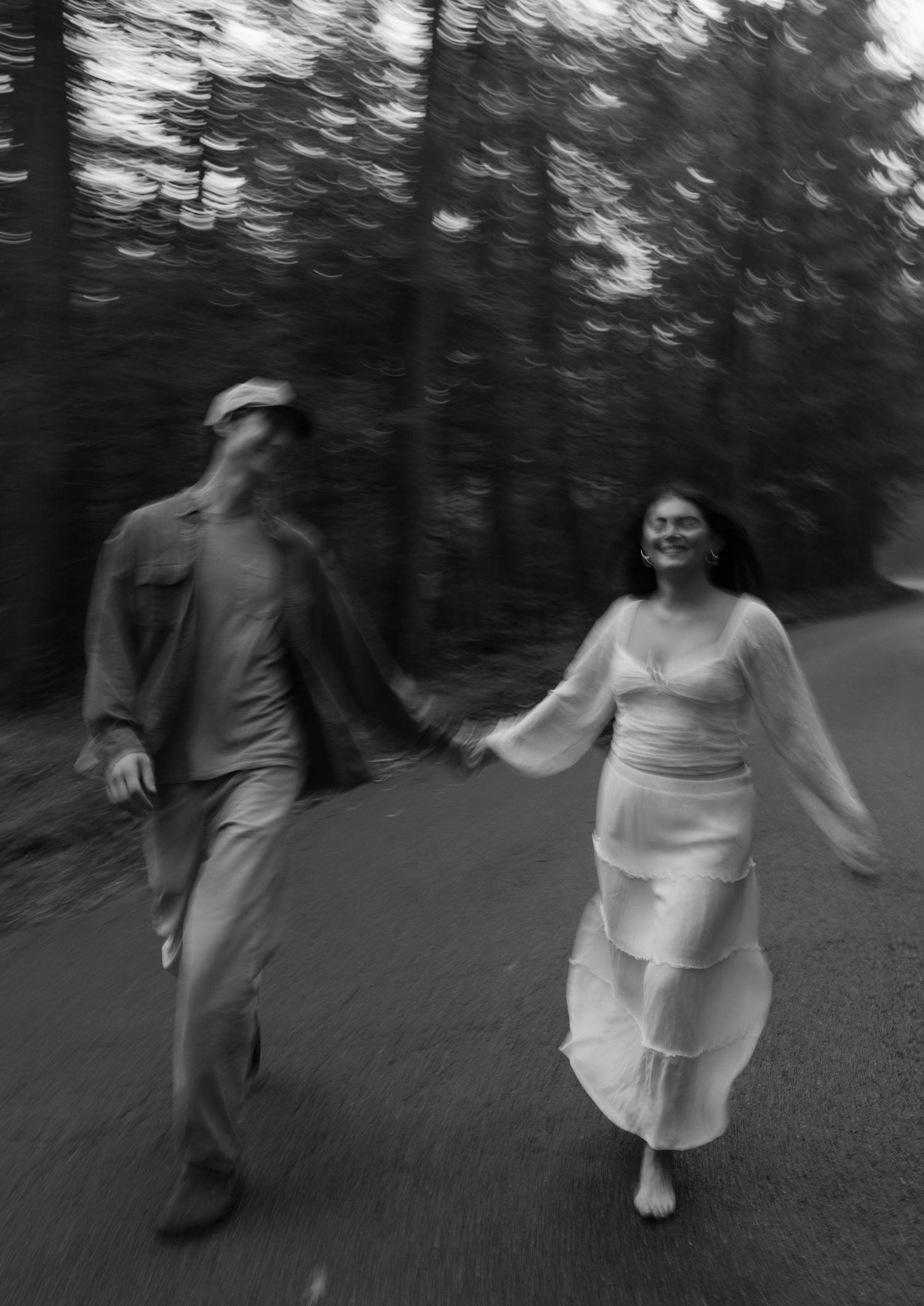 Motion-blurred black and white photograph of people dancing on a forest path.