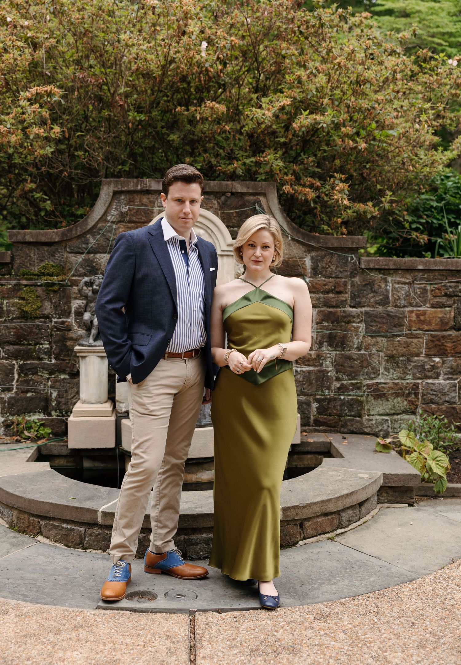 Couple posing in front of stone fountain garden, woman in green satin dress, man in navy blazer and khakis.