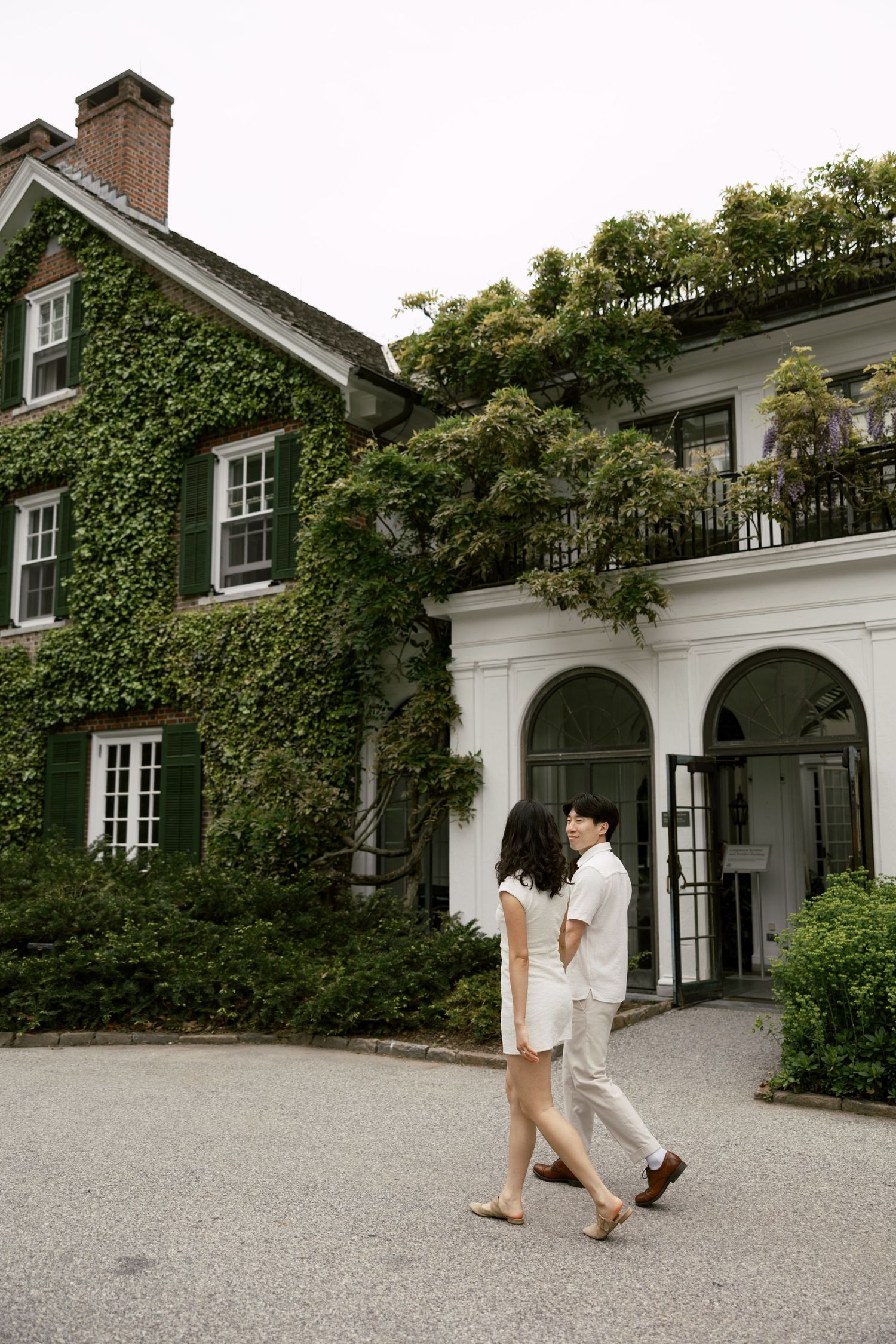 Couple walking along a beautiful ivy-covered mansion with white exterior.