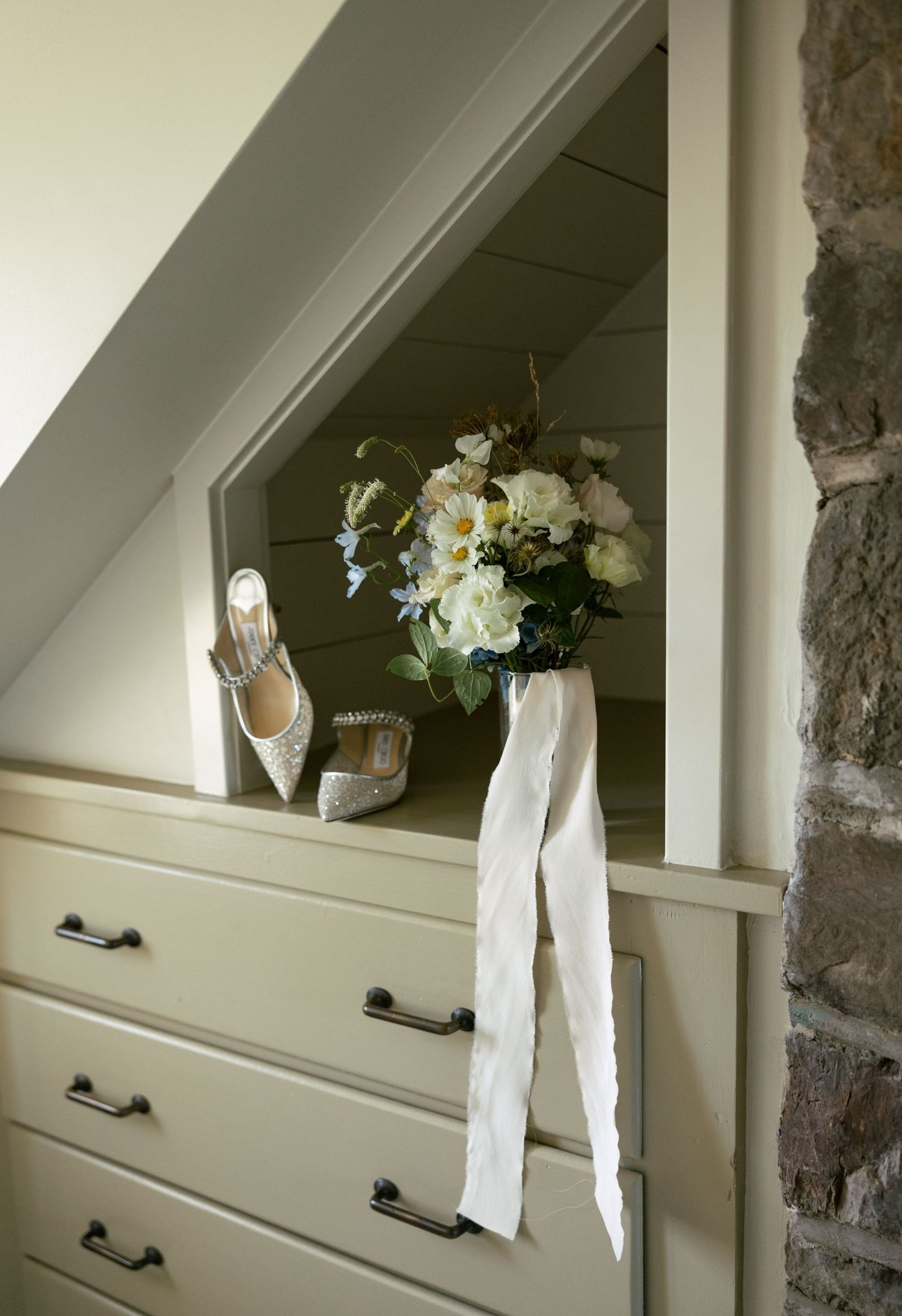 Wedding details including bridal bouquet, white shoes, and dress displayed on a dresser.