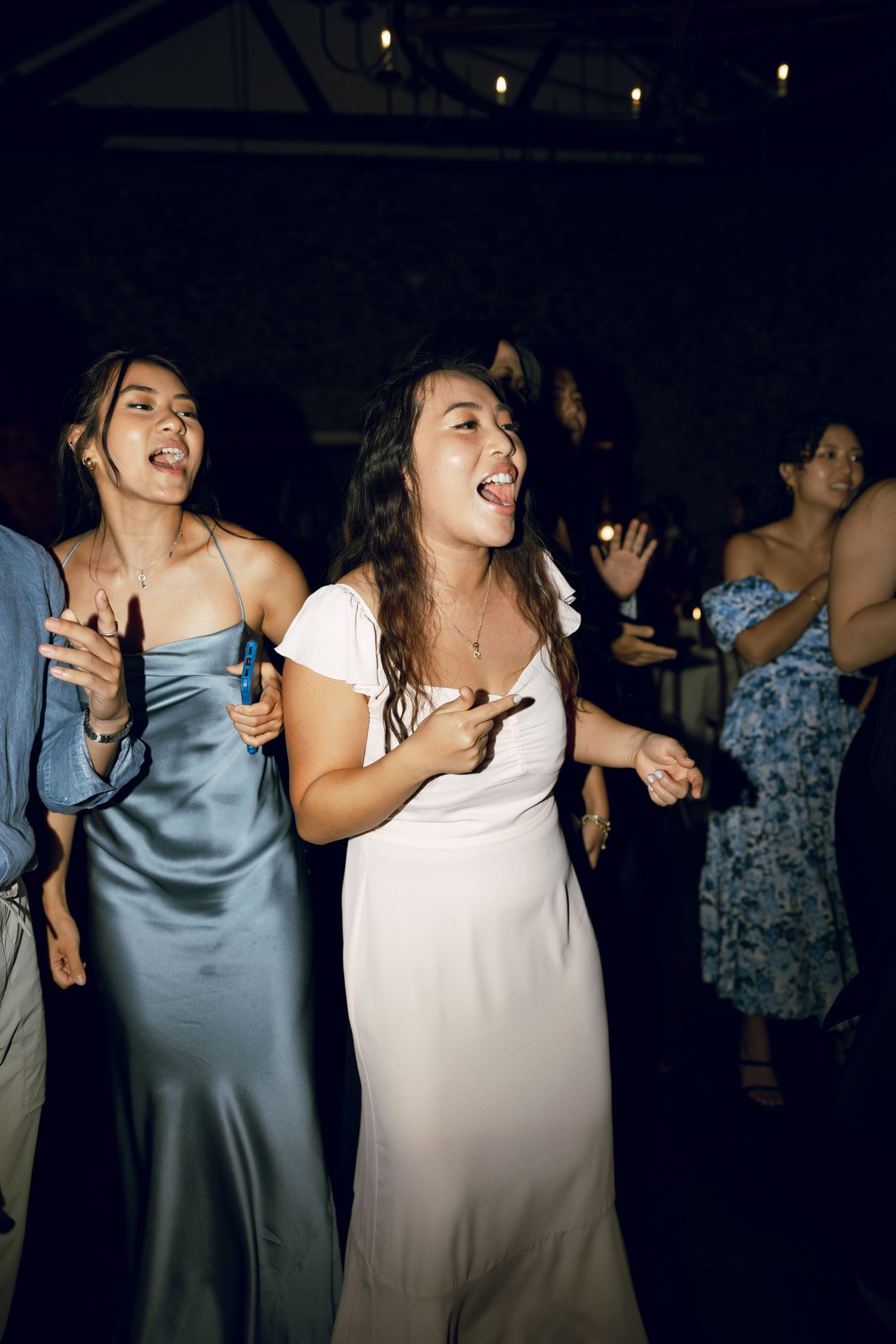 Wedding guests dancing and celebrating at a dimly lit reception venue.