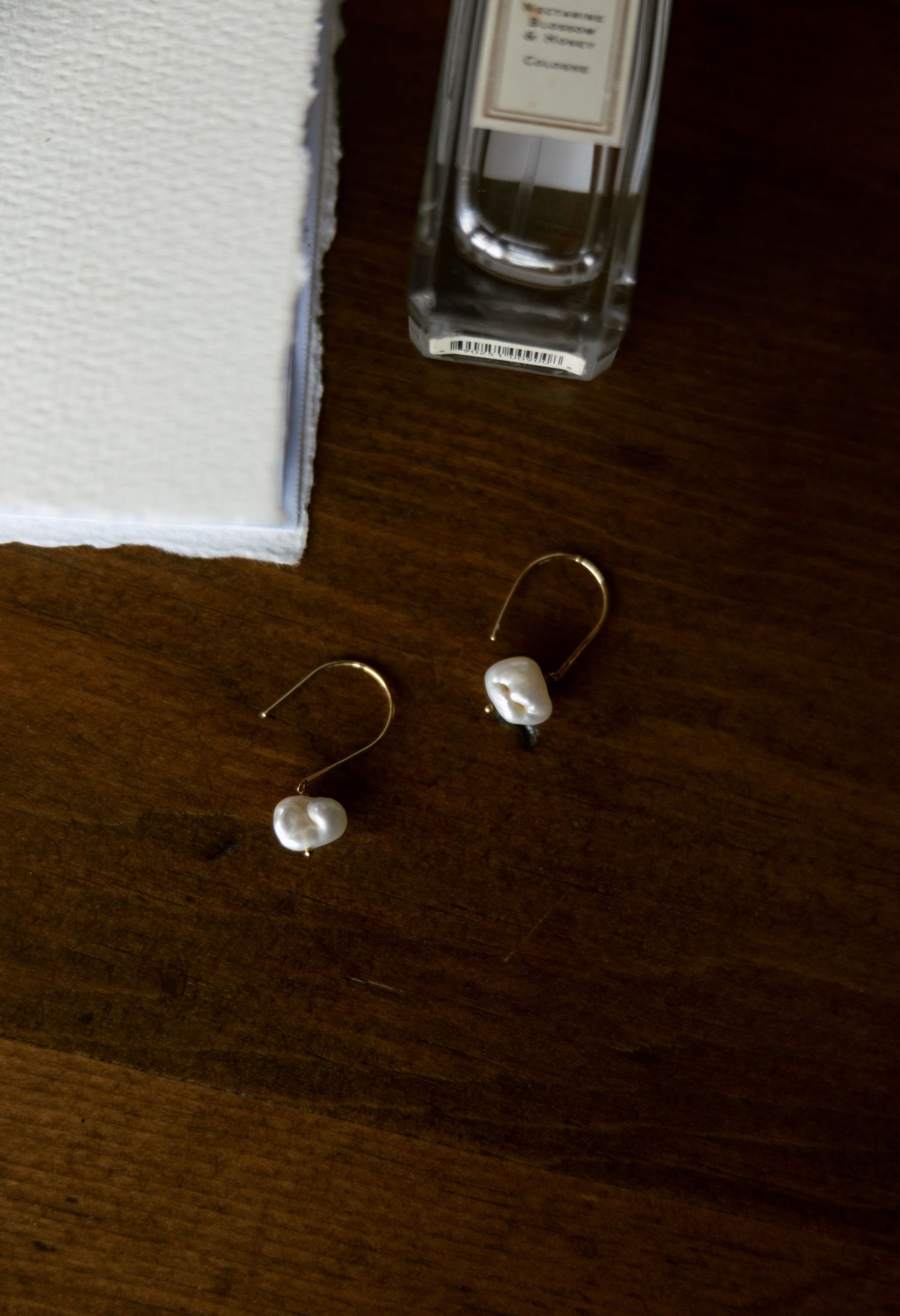 Pearl drop earrings and perfume bottle on a dark wooden surface.