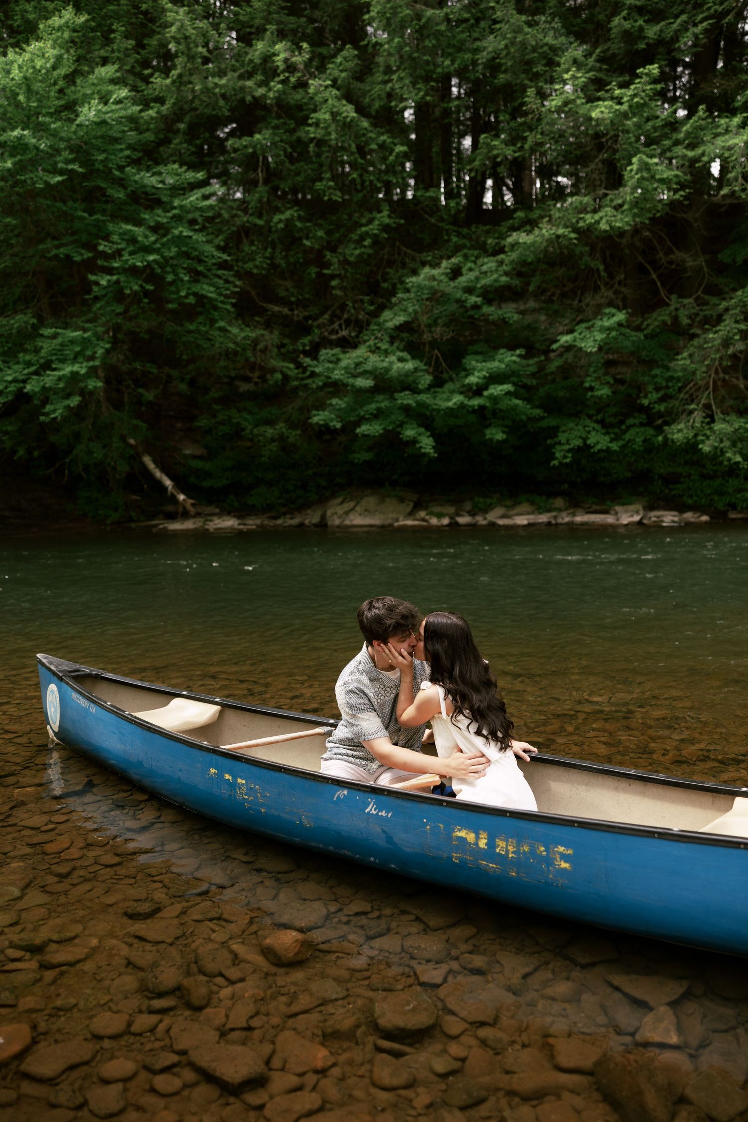Couple sharing an intimate moment in a blue canoe on a peaceful river.