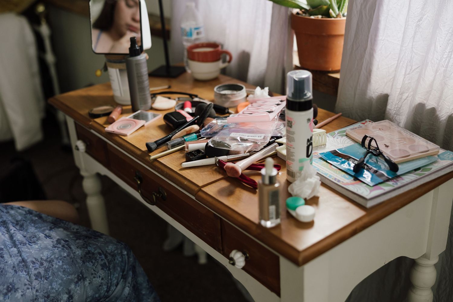 A cluttered wooden desk surface with various personal items and decor in natural lighting.