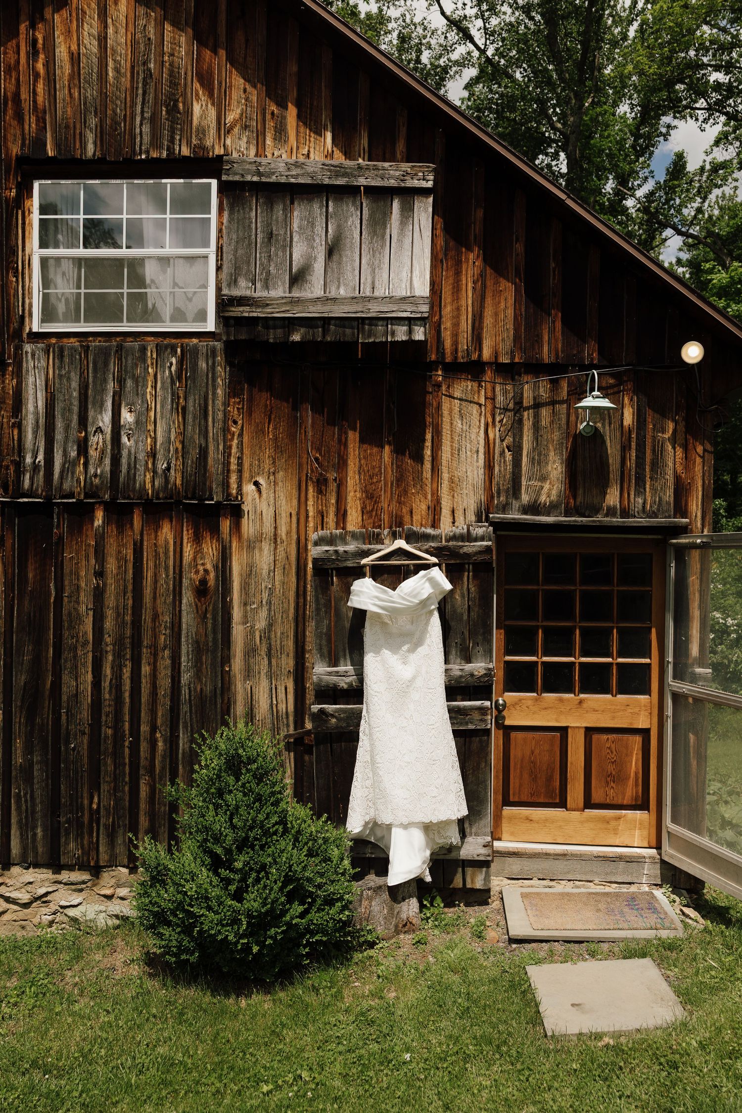 A white wedding dress displayed outside a rustic wooden barn with vintage windows.
