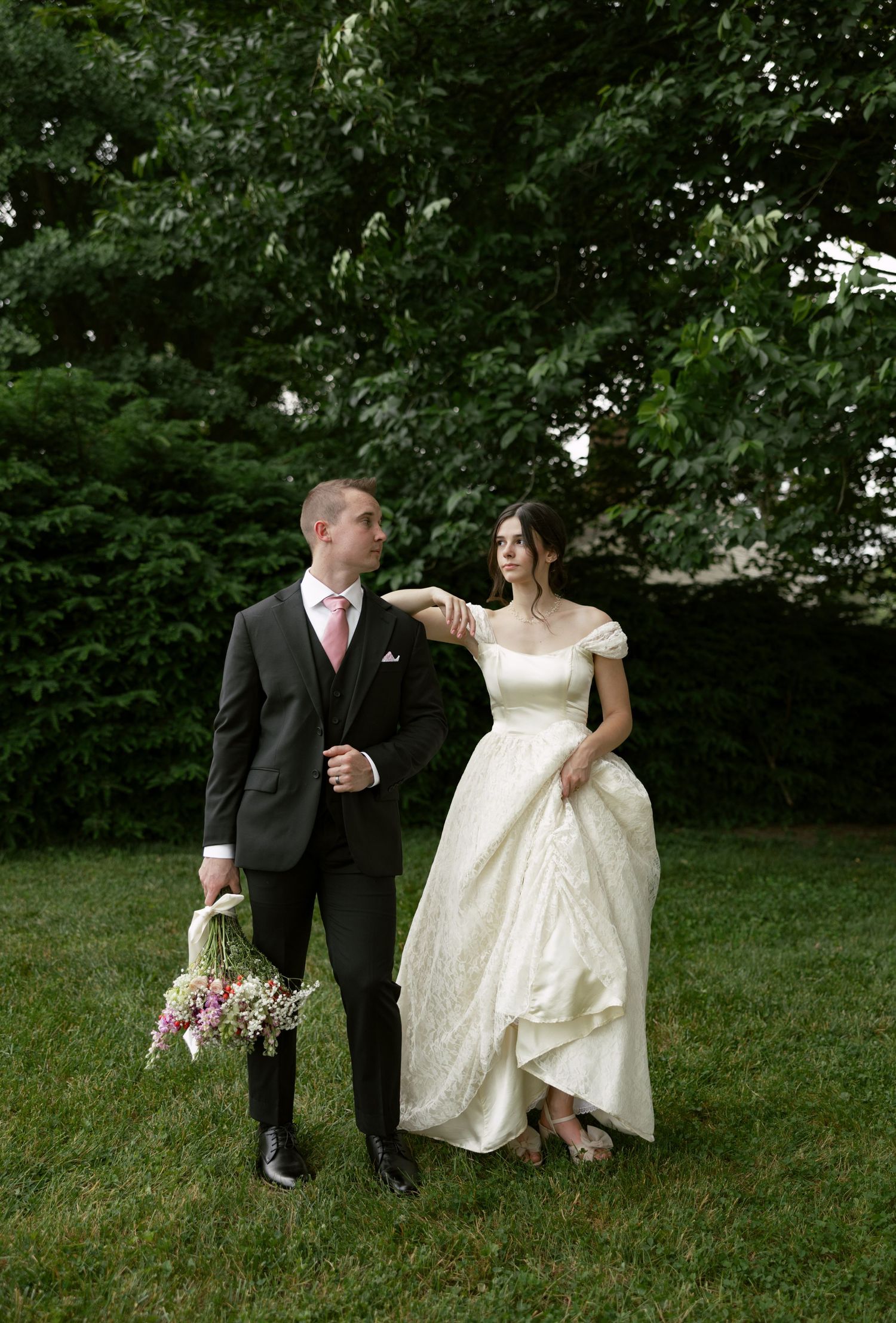Wedding couple walking and posing playfully on a lush green lawn.