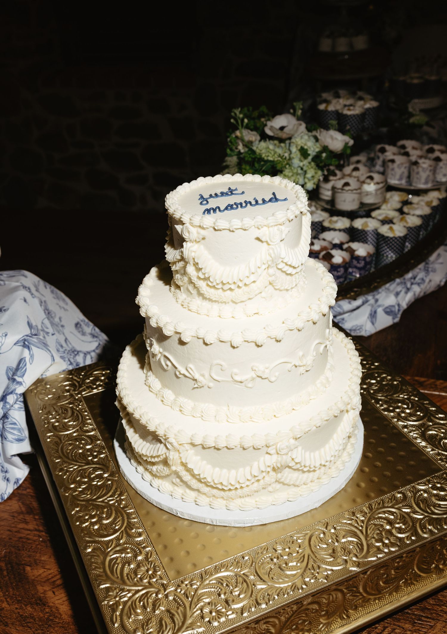 A white three-tiered wedding cake with delicate piped details displayed on a decorative gold serving platter.