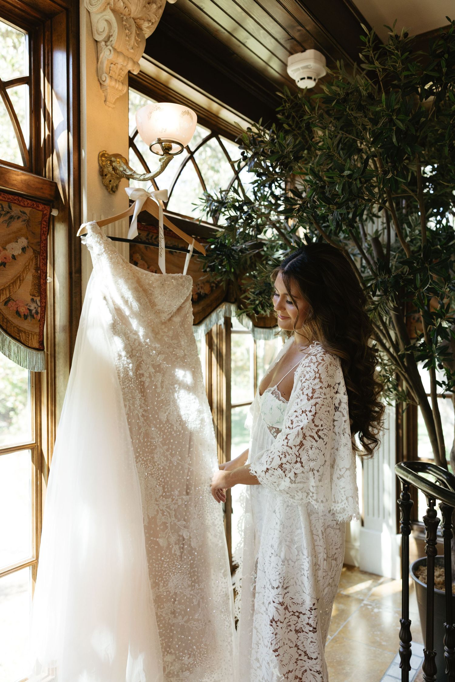 White lace wedding dresses hanging on display in a sunlit room with green plants and natural decor.