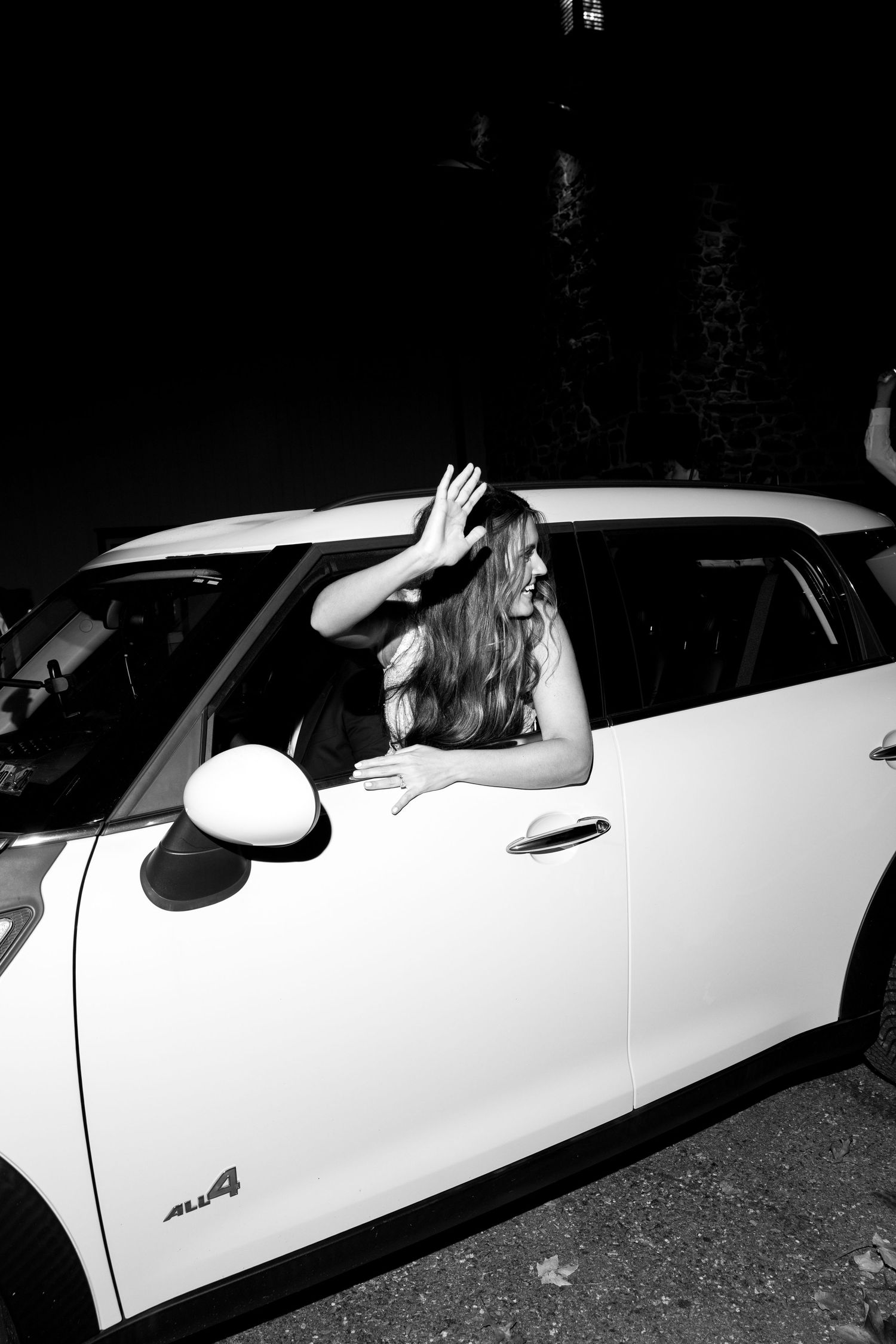 A white car is parked at night with someone entering through the passenger side door.