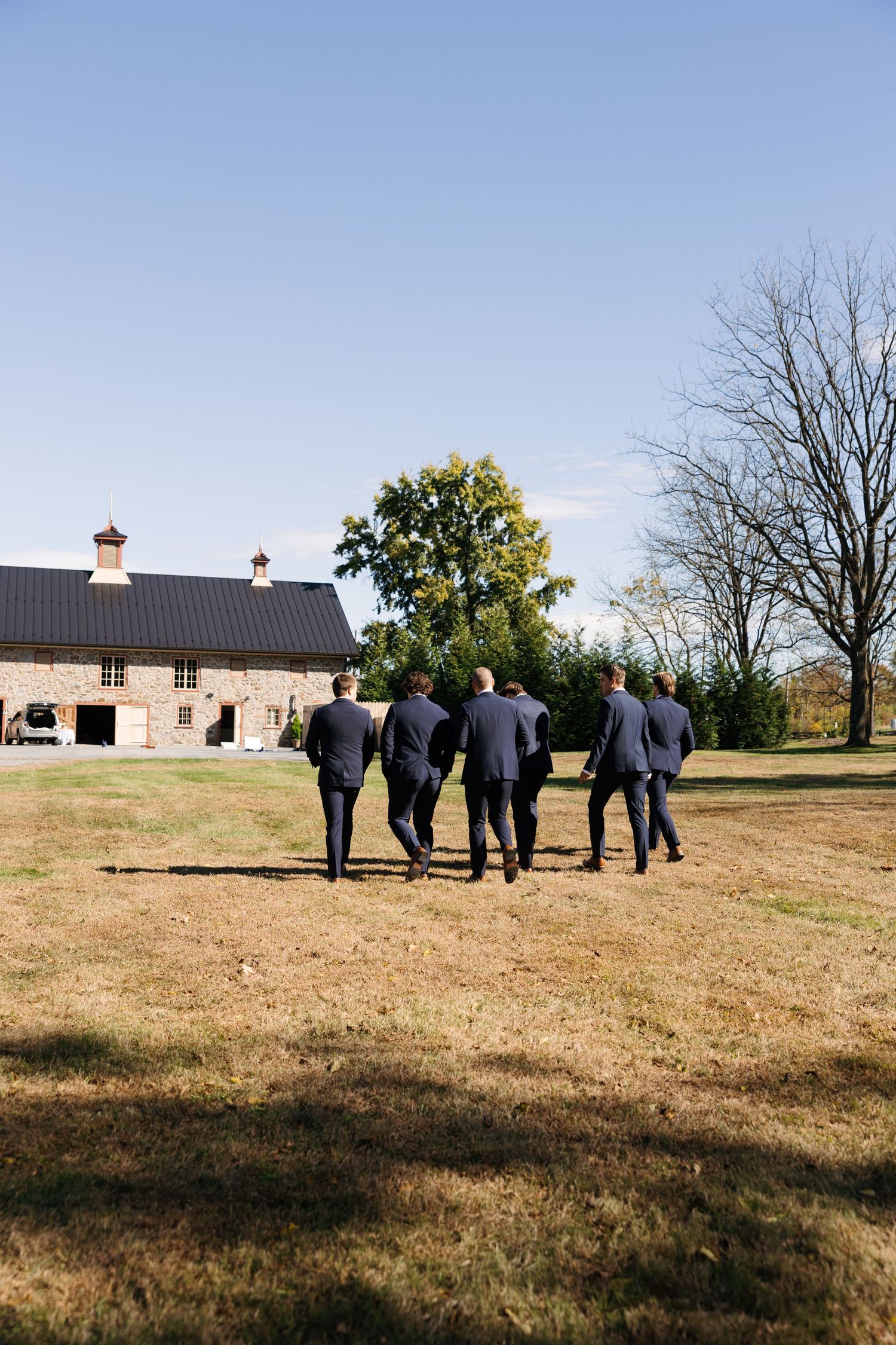 Group walking across a grassy hilltop field towards a rustic stone building on the horizon.